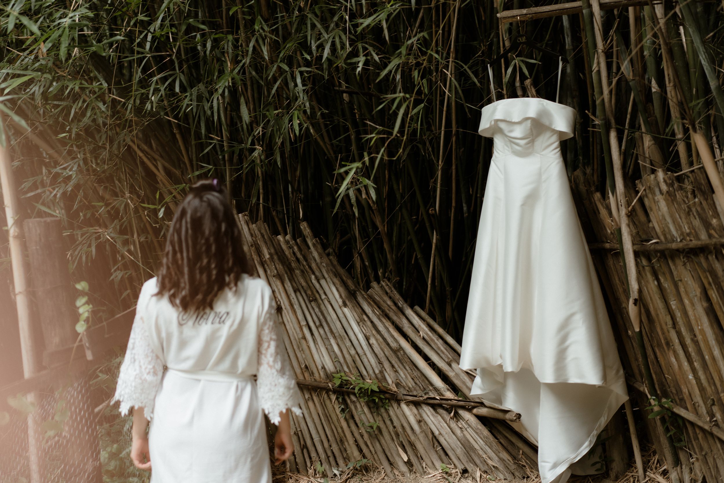 White wedding dress hanging against natural bamboo backdrop.