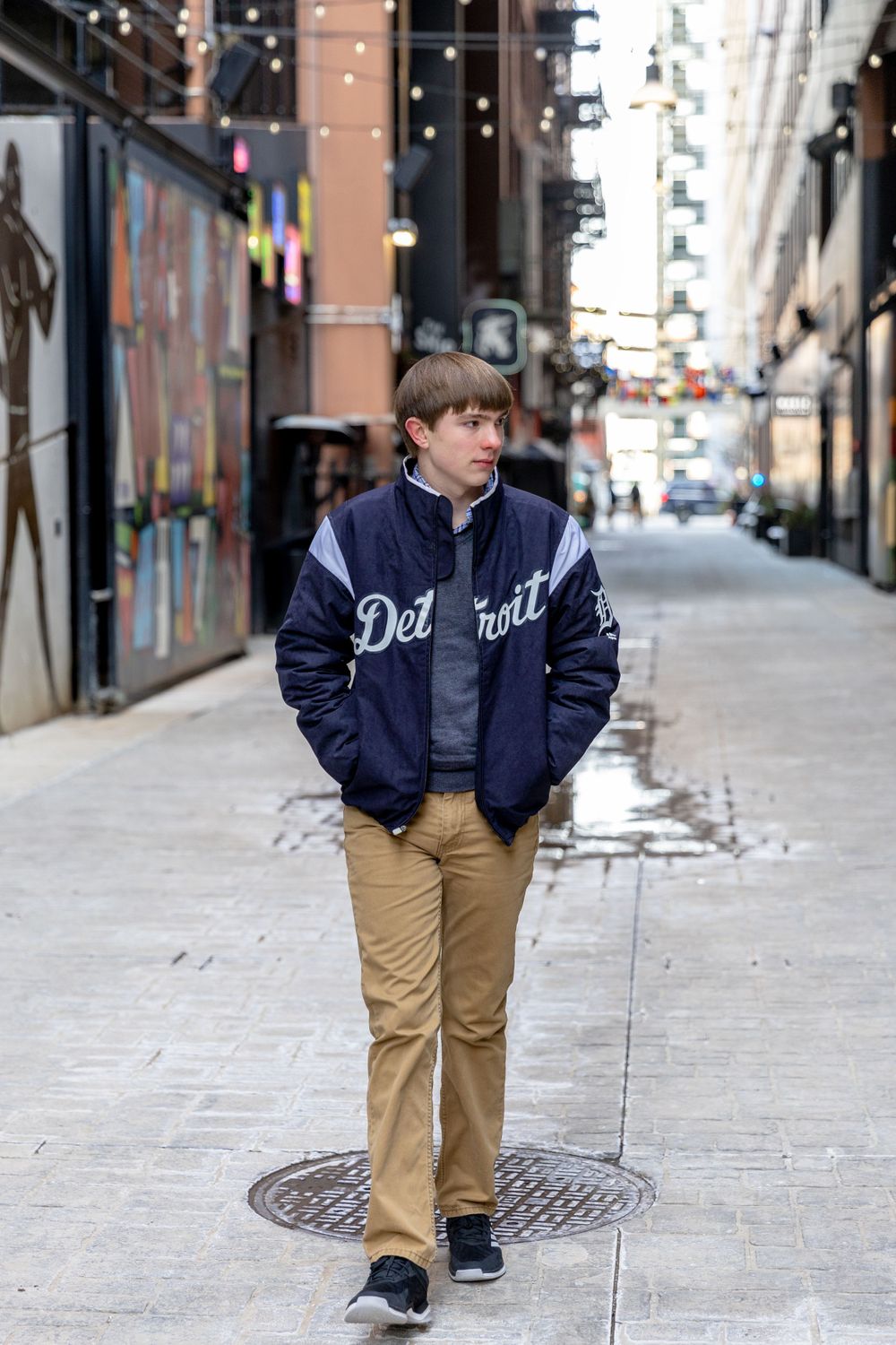 teenage boy wearing a detroit varsity jacket walking down the sidewalk in Downtown Detroit