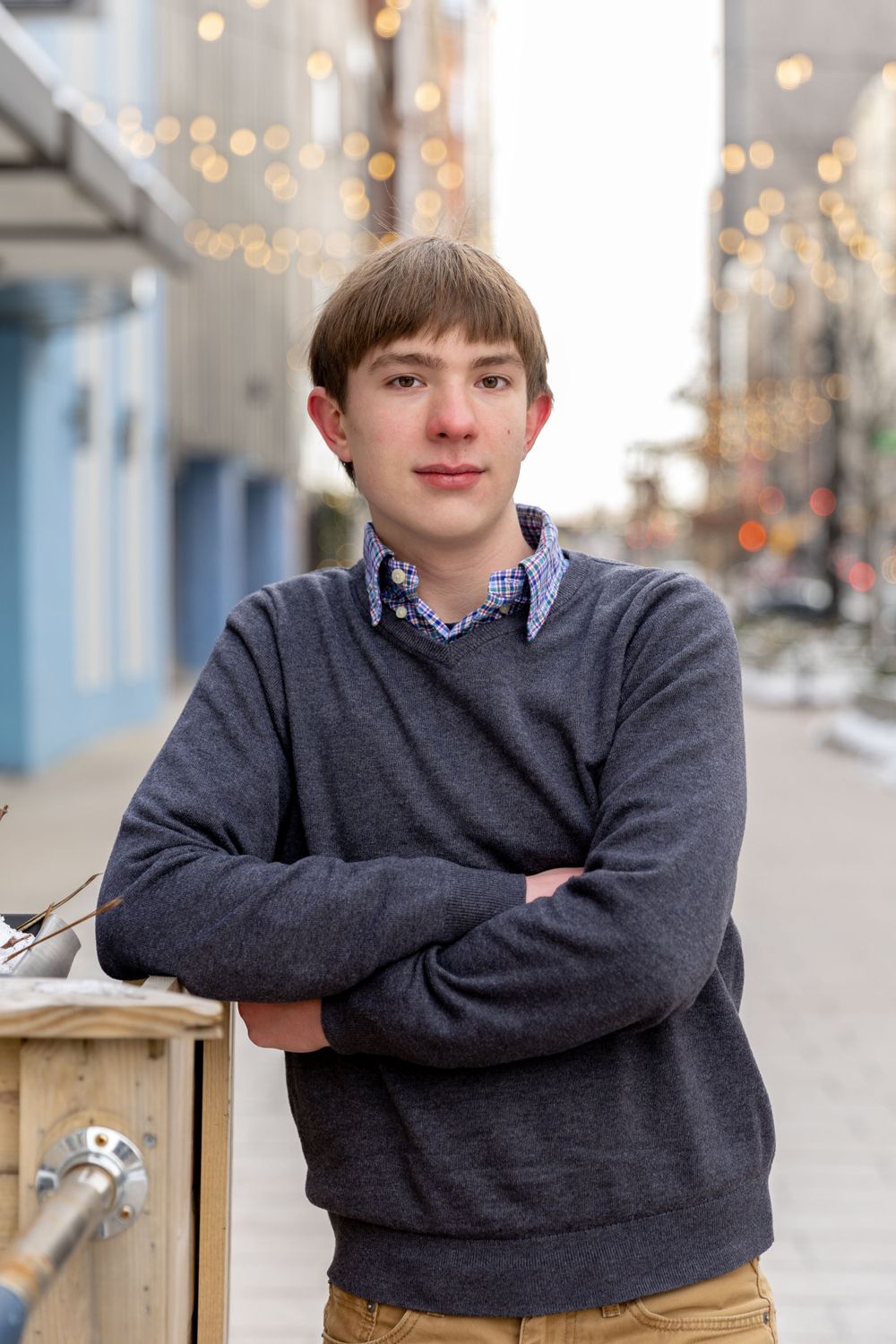 teenage boy in a blue sweater leaning against a fence with christmas lights behind him in downtown detroit