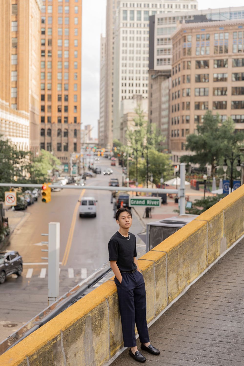 teenage boy leans on the edge of a rooftop for a photo in downtown Detroit