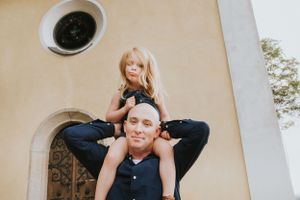 Smiling bald man carrying young blonde girl on his shoulders outside a church.