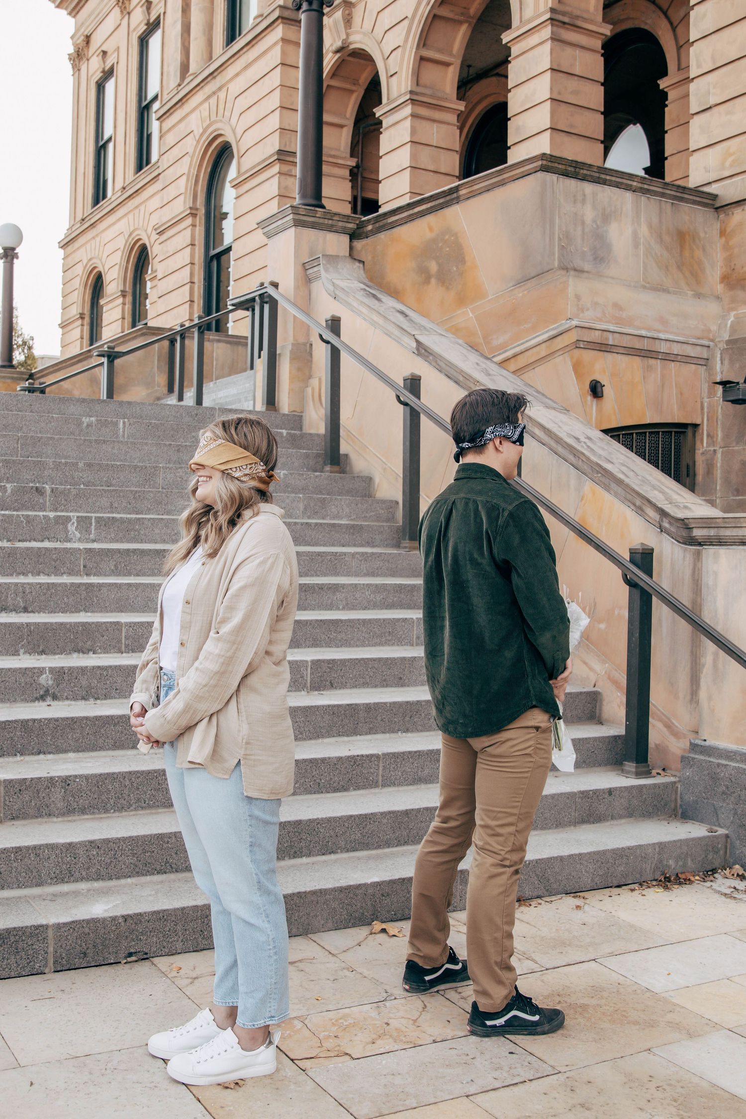 Two people stand on historic stone building steps with arched architecture.