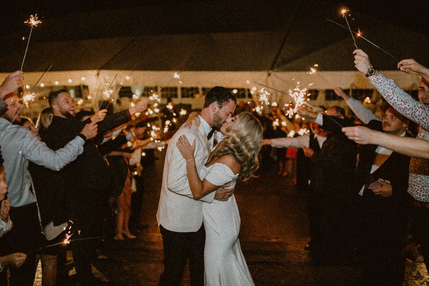 A romantic wedding exit with guests holding sparklers during an evening celebration.