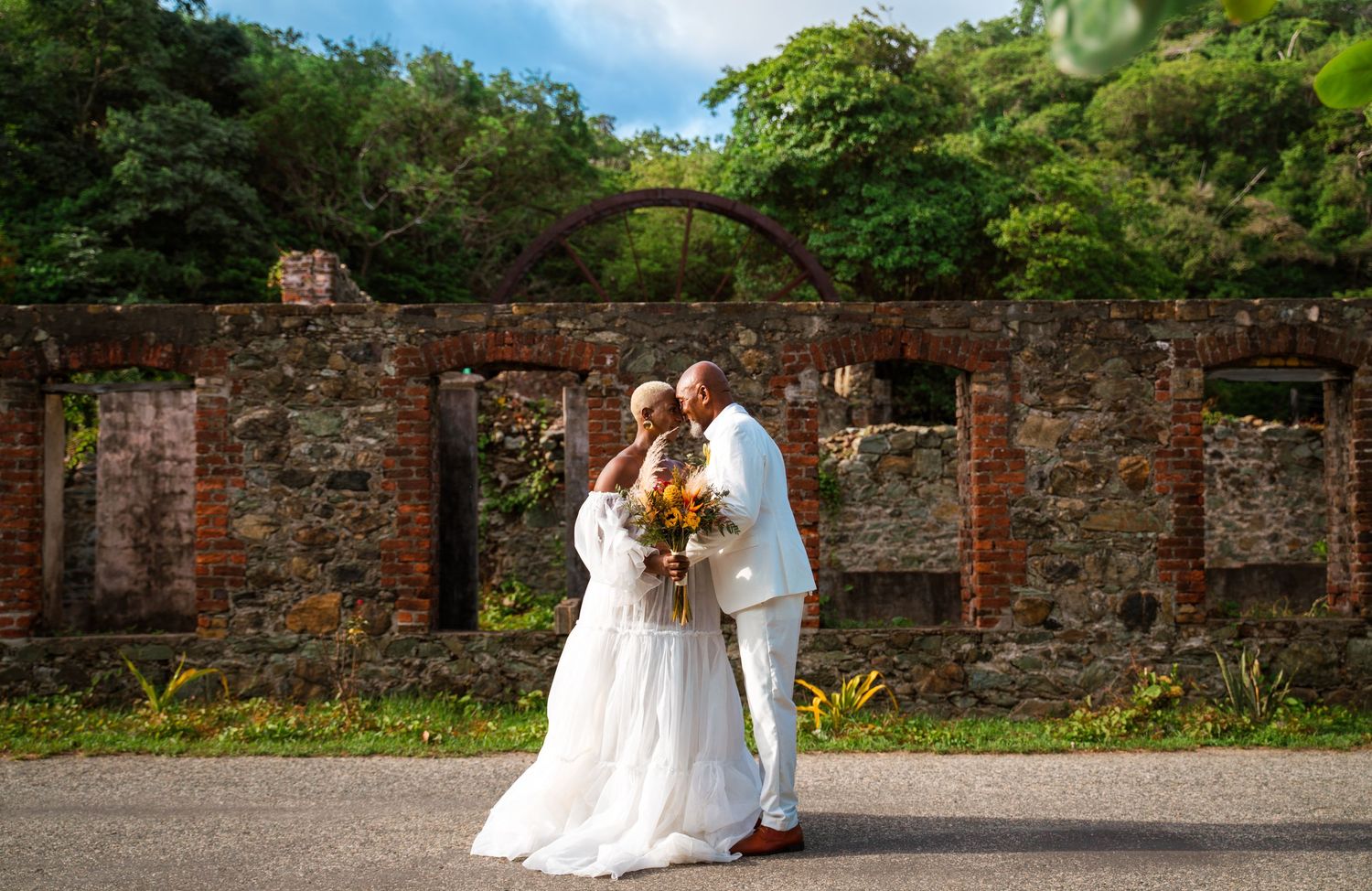 A wedding portrait against rustic brick ruins surrounded by lush greenery.