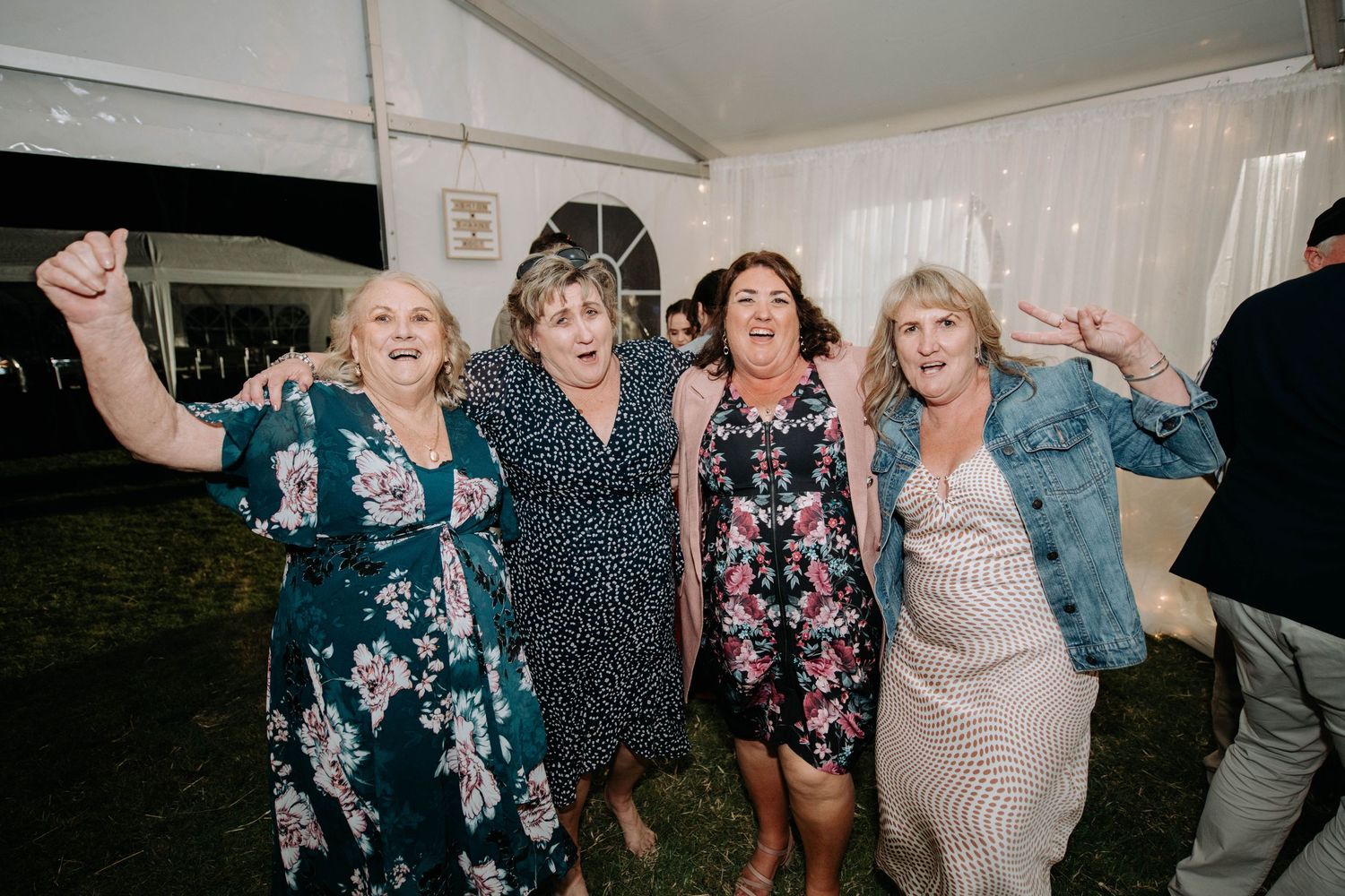 Four women in floral dresses dancing and celebrating joyfully at a wedding reception.