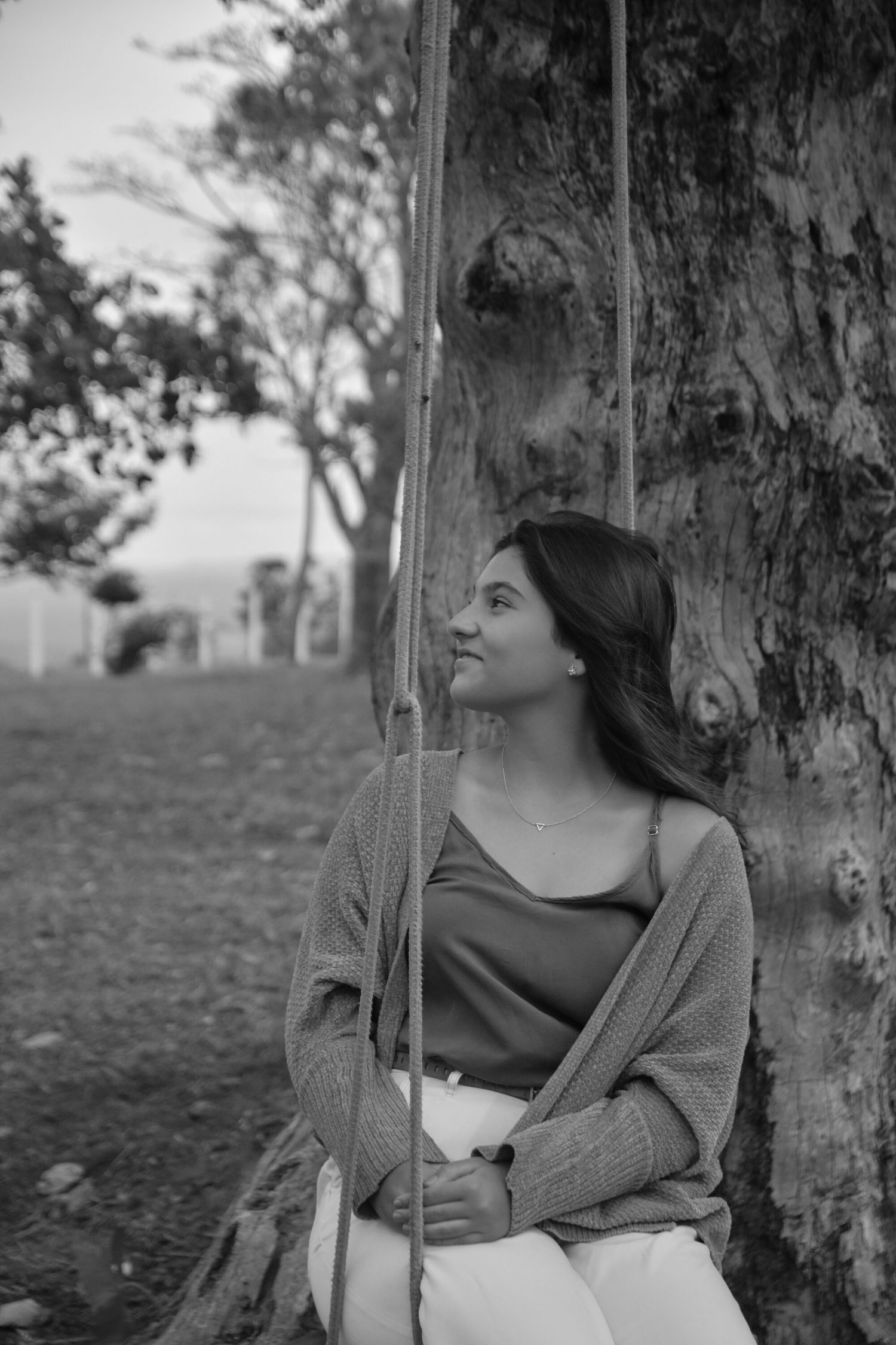 A thoughtful black and white portrait of someone sitting on a tree swing.