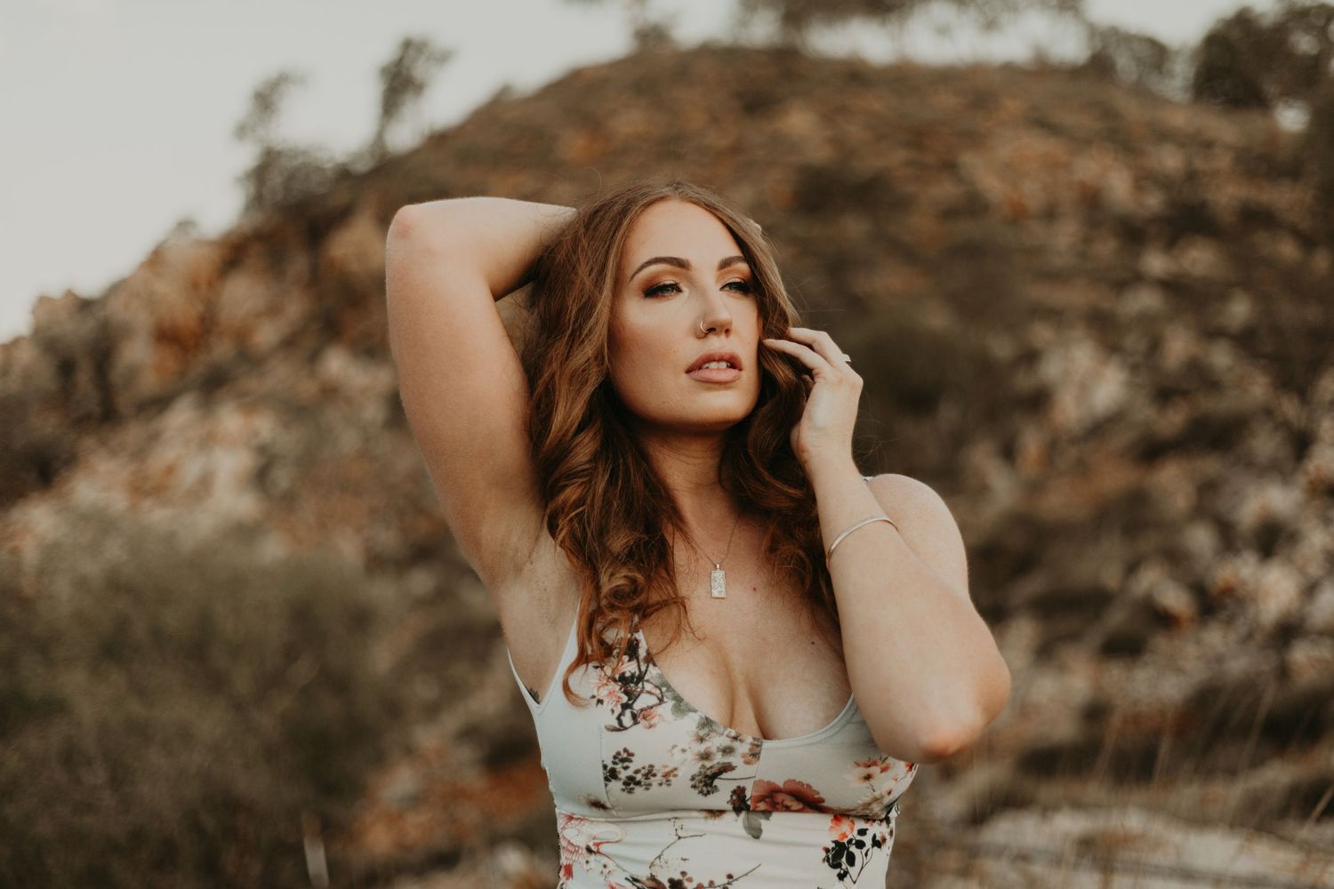 Woman with hand on head and collarbone posing in front of hills at Lake Moondarra in Mount Isa