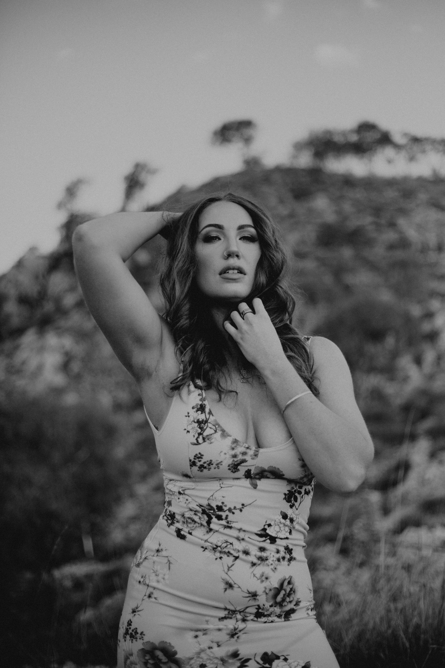 Woman with hand on head and collarbone posing in front of hills at Lake Moondarra in Mount Isa