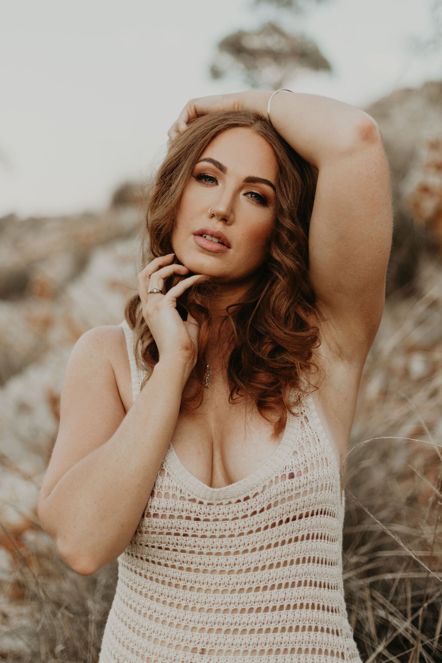 Woman with hand on cheek and collarbone posing in front of hills at Lake Moondarra in Mount Isa