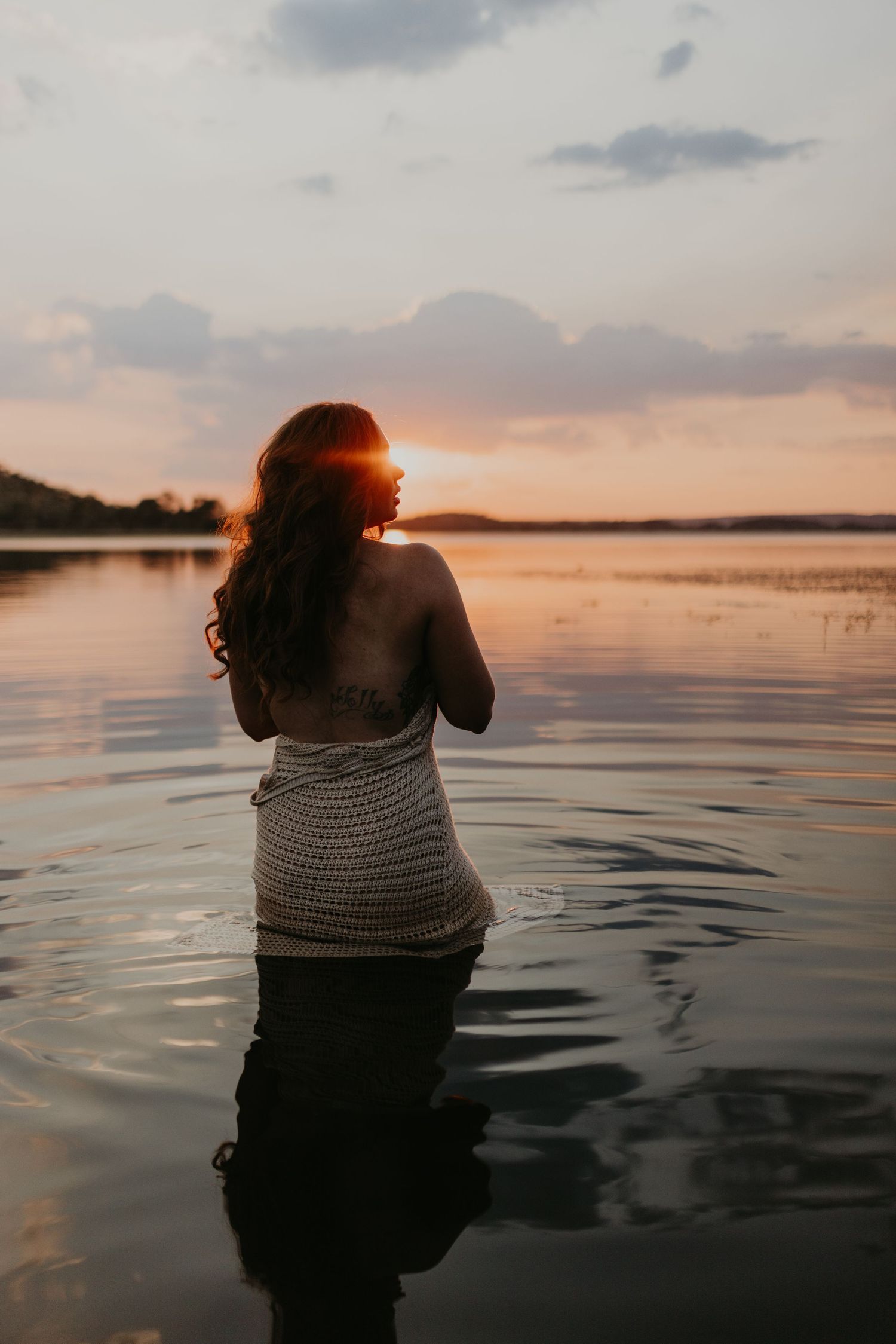Woman standing in water at Lake Moondarra, Mount Isa with sunset behind her