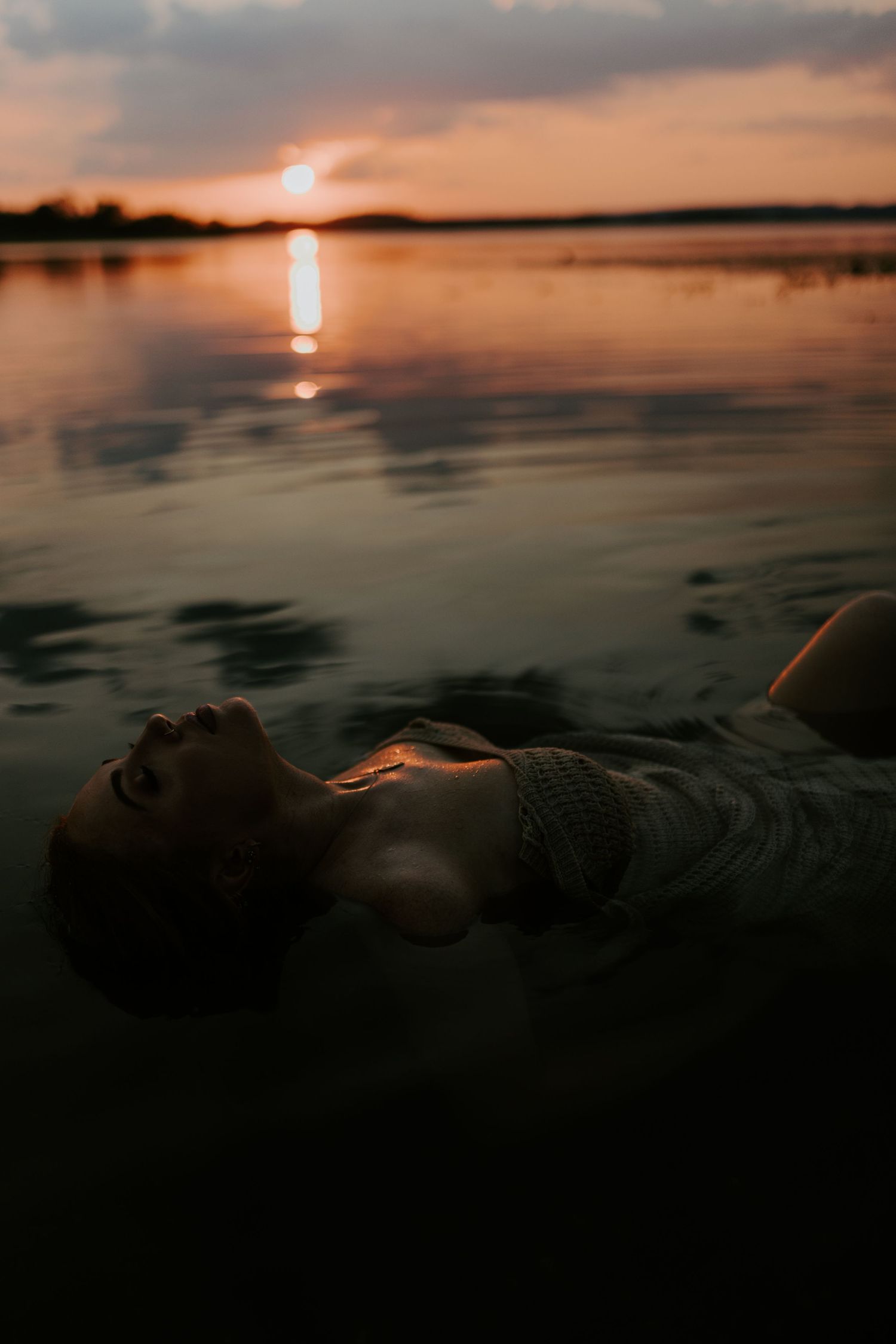 Woman caressing her face in water at Lake Moondarra, Mount Isa with sunset behind her