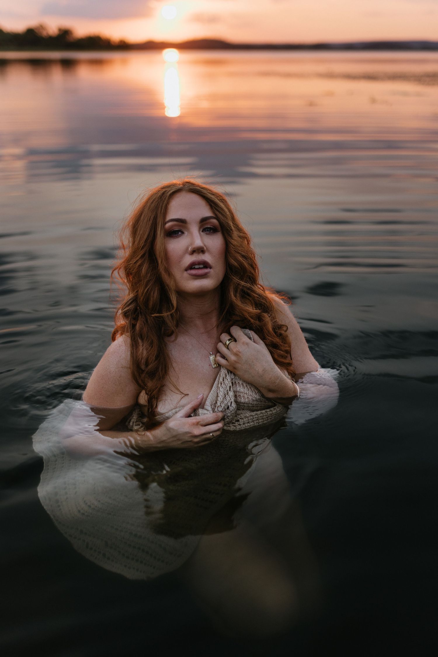Woman caressing her face in water at Lake Moondarra, Mount Isa with sunset behind her