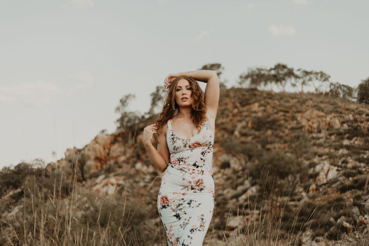 Woman with hand on head and collarbone posing in front of hills at Lake Moondarra in Mount Isa