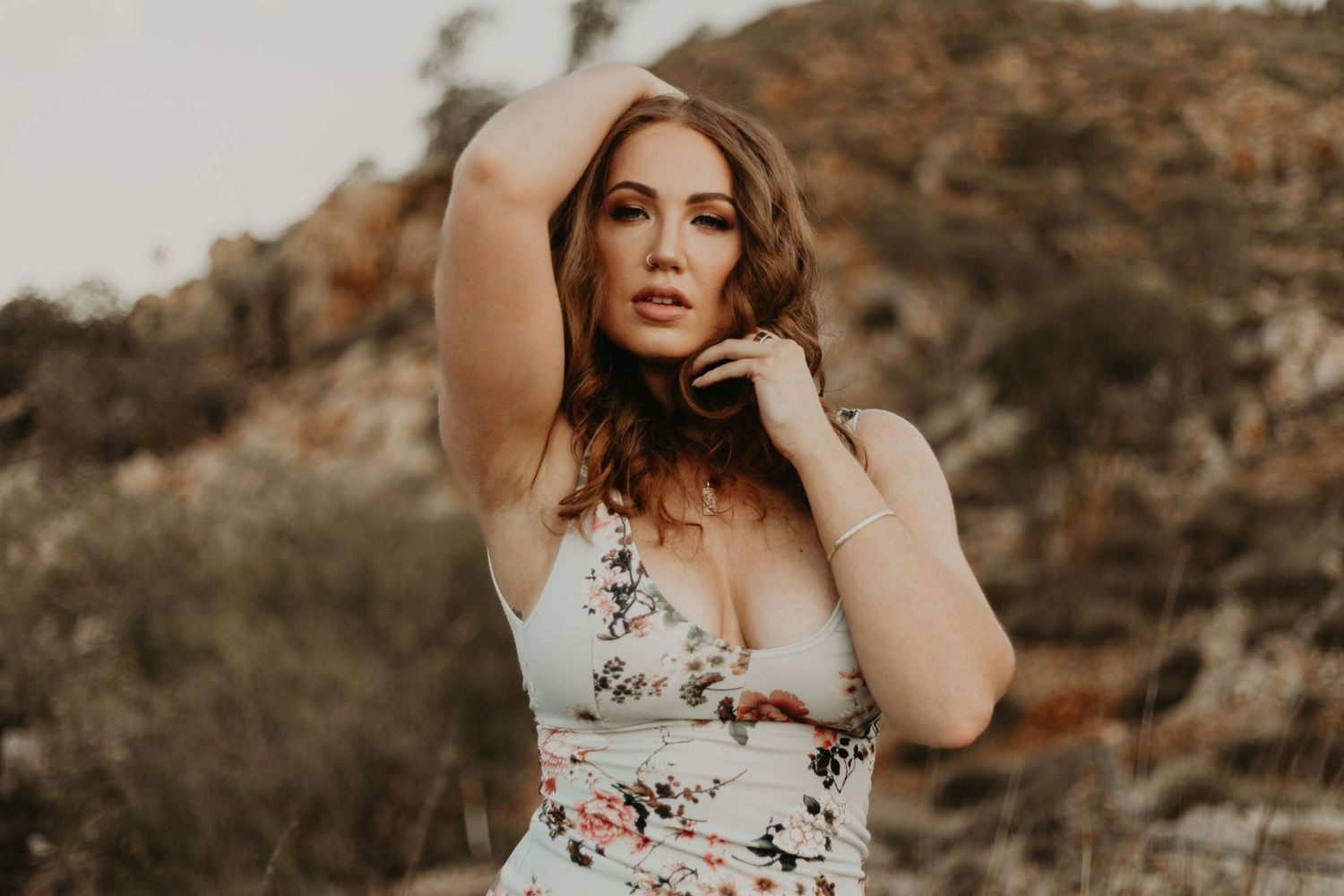 Woman with hand on head and collarbone posing in front of hills at Lake Moondarra in Mount Isa