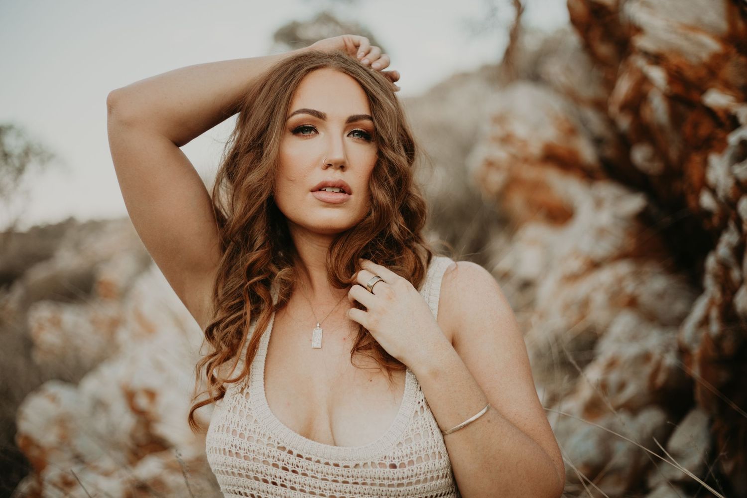 Woman with hand on head and collarbone posing in front of hills at Lake Moondarra in Mount Isa