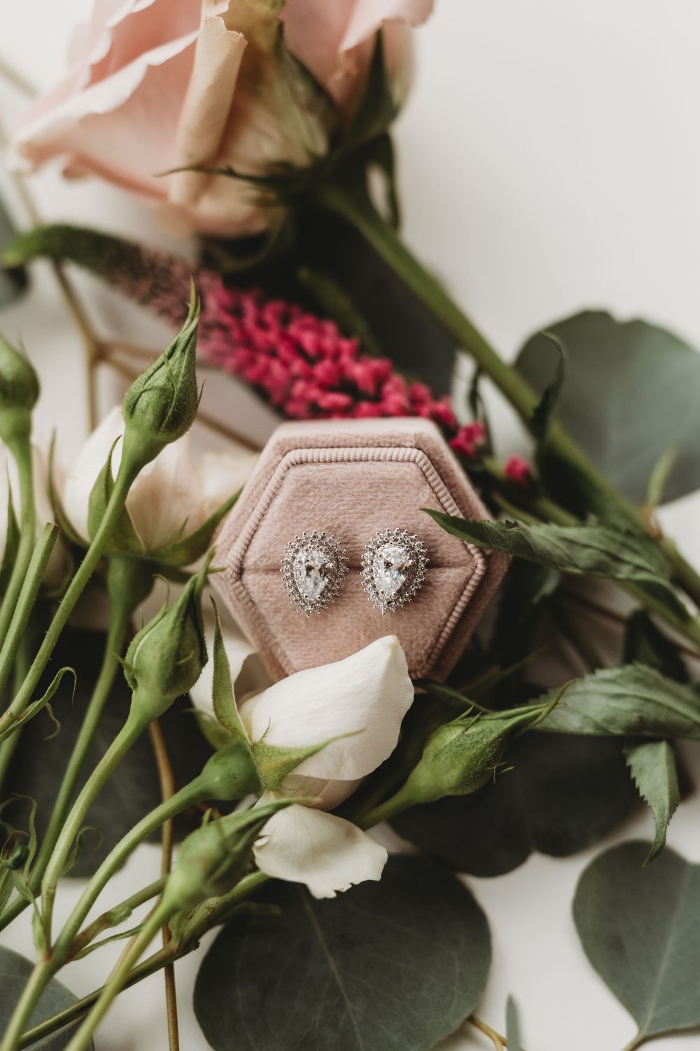 Elegant teardrop-shaped diamond earrings displayed on a velvet box with roses and greenery.
