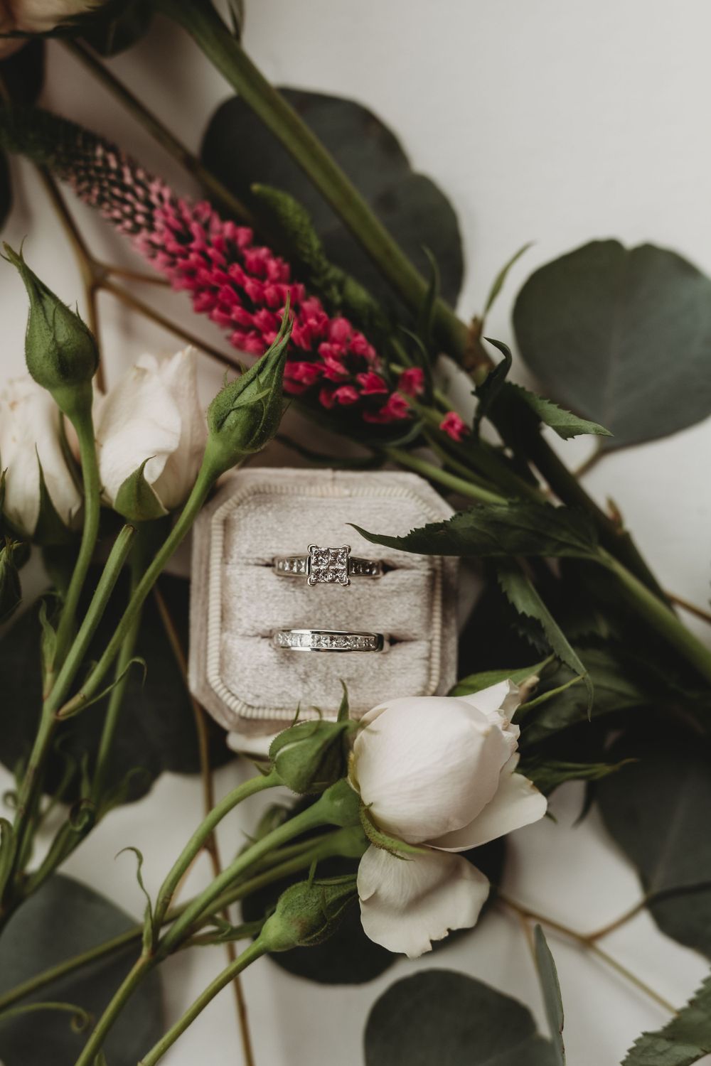 Wedding rings nestled among white roses and pink flowers with greenery.