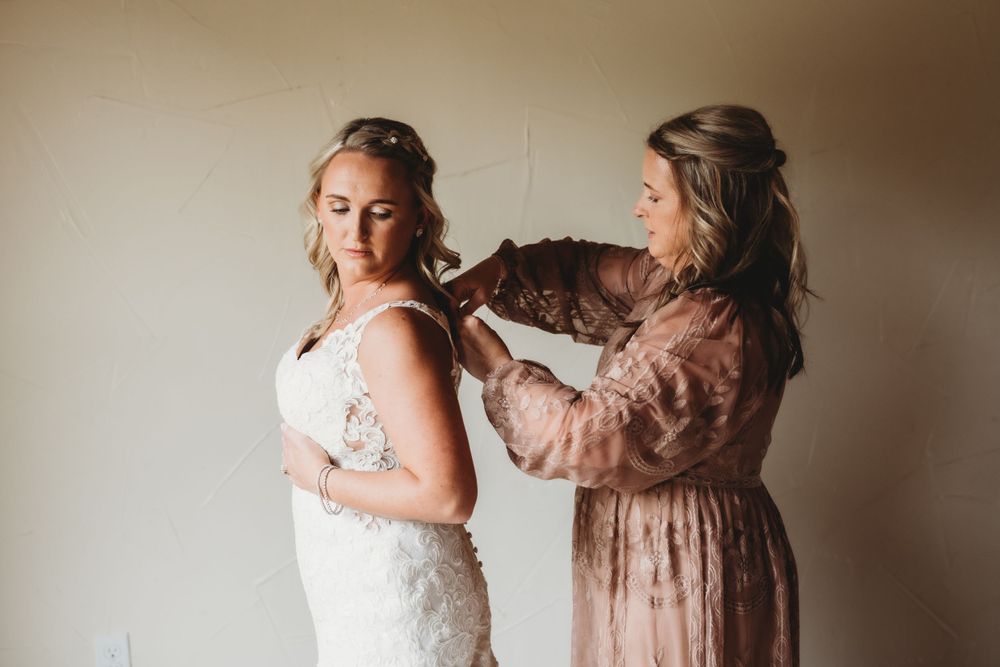 Helper assists with final wedding dress preparations against neutral backdrop.