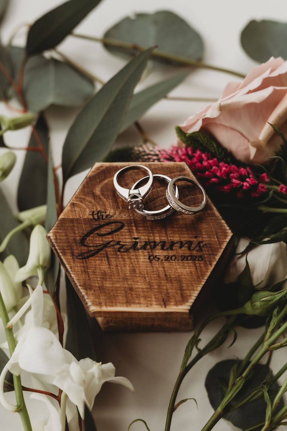Wedding rings on a wooden hexagonal box decorated with roses and eucalyptus leaves.