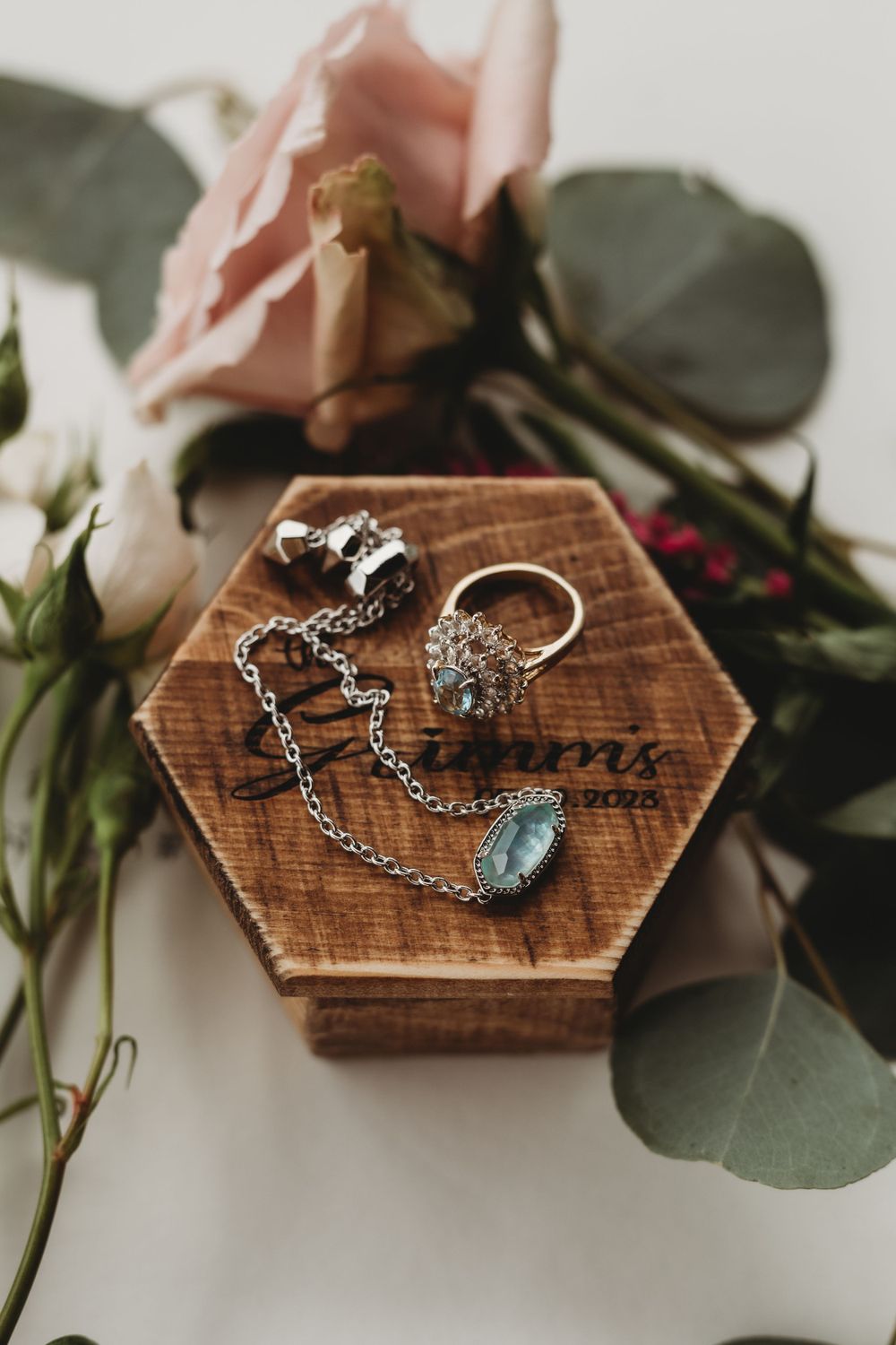 Wedding jewelry and rings displayed on a wooden hexagon box surrounded by flowers.