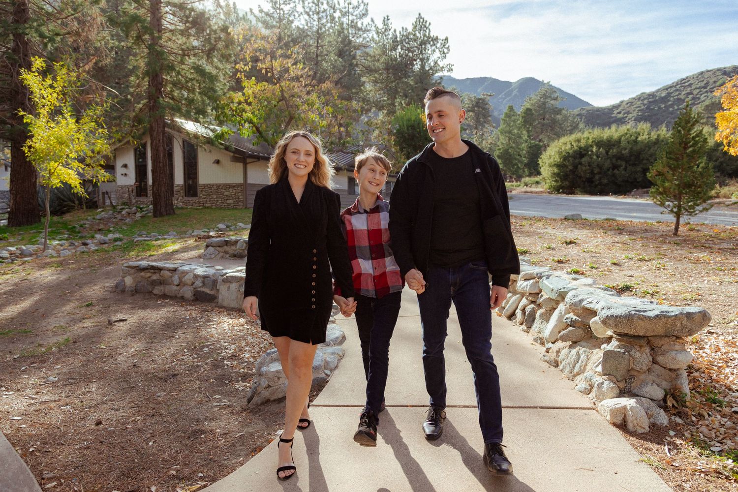Three people posing on a stone pathway with mountains visible in background.