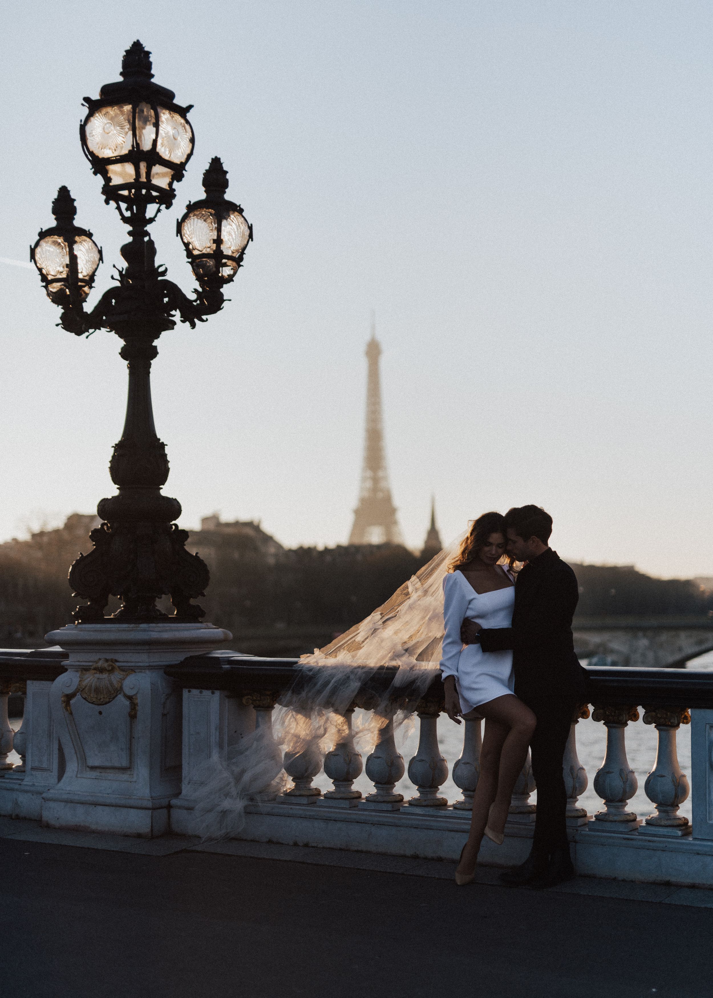 Silhouettes against a Parisian skyline with ornate lampposts and stone balustrades.