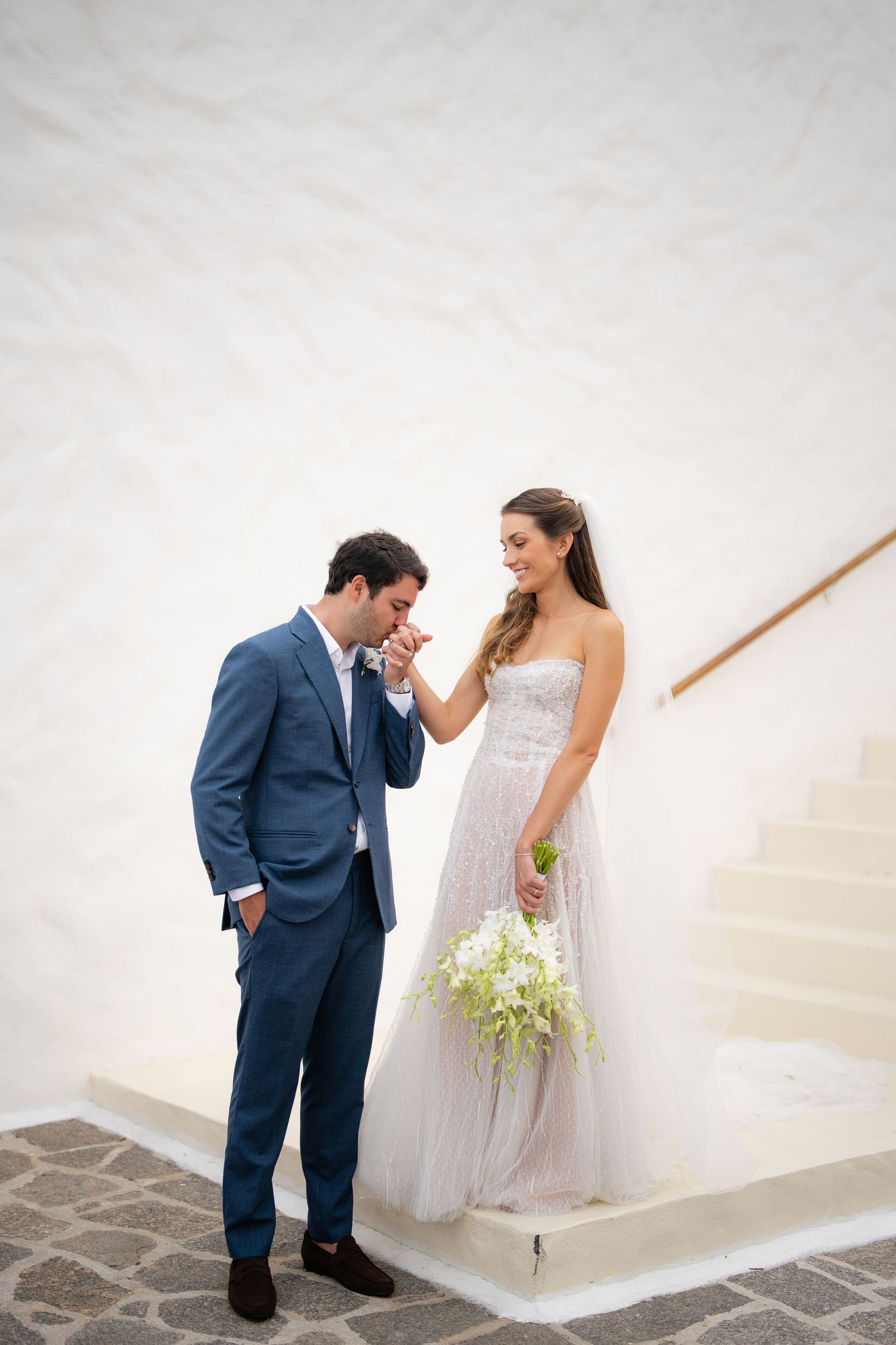 Meeting moment captured on white staircase with elegant wedding attire.