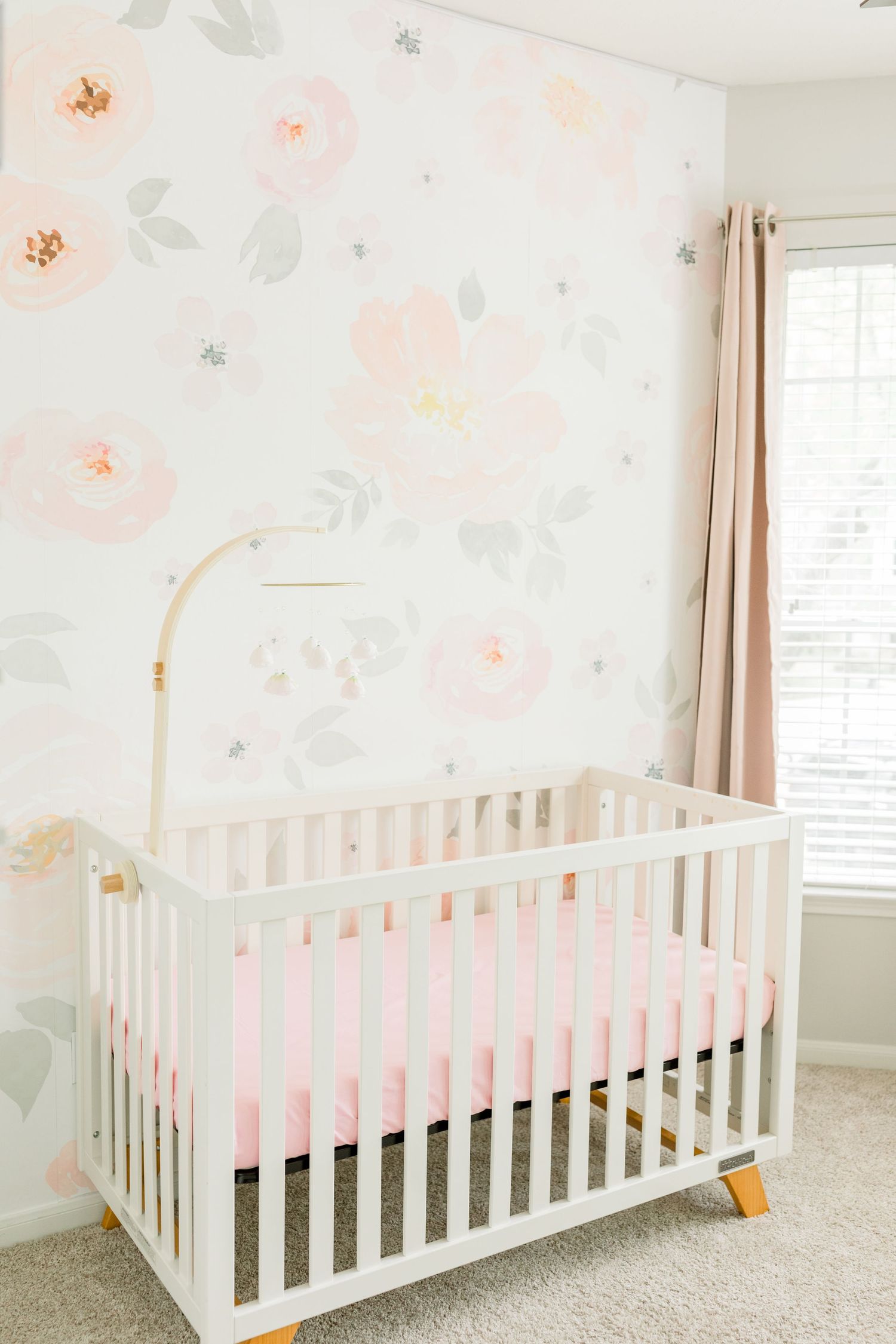 Modern nursery with white crib and delicate floral wallpaper in soft peach and gray tones.