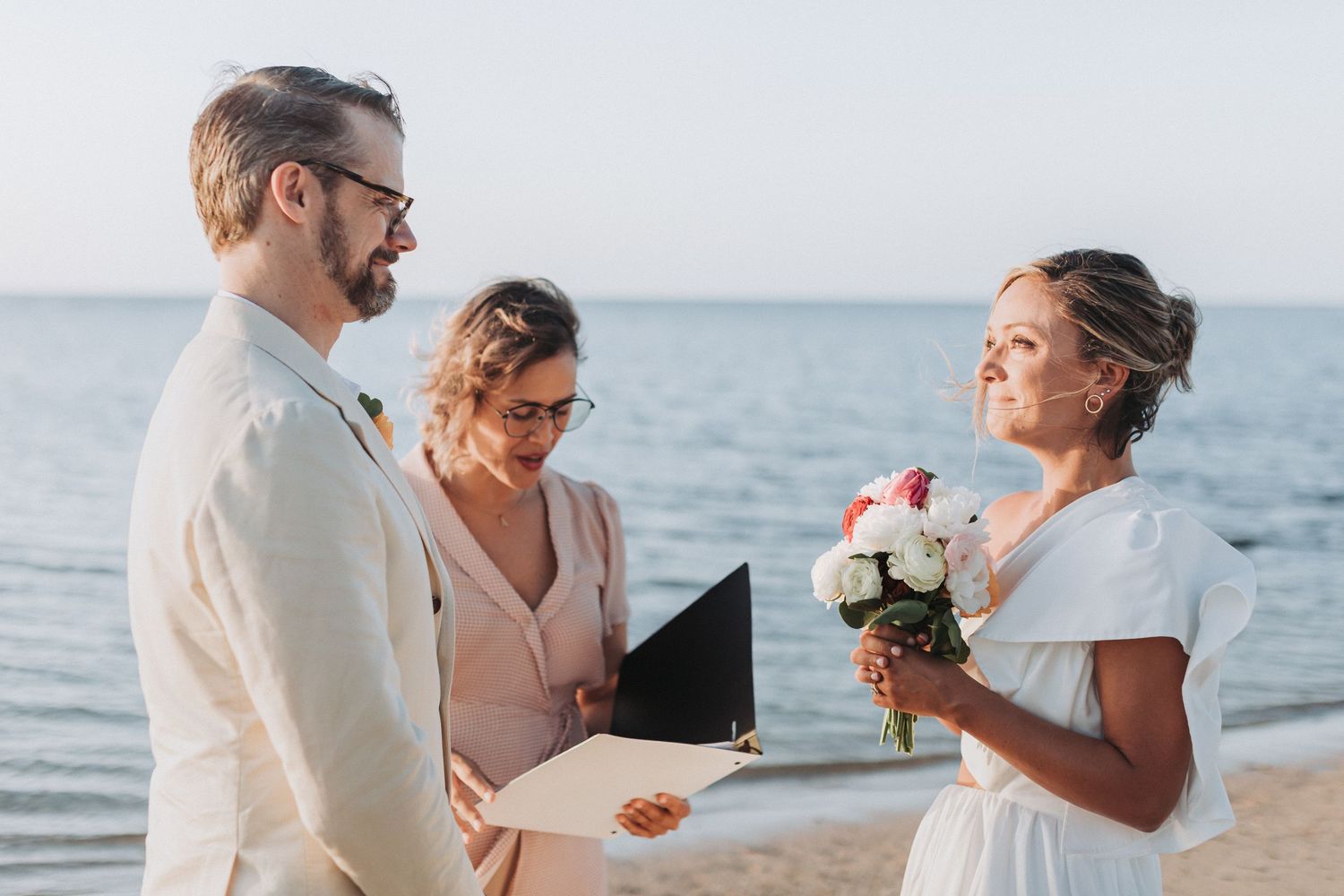 Intimate beach wedding ceremony with officiant and couple exchanging vows by the ocean.