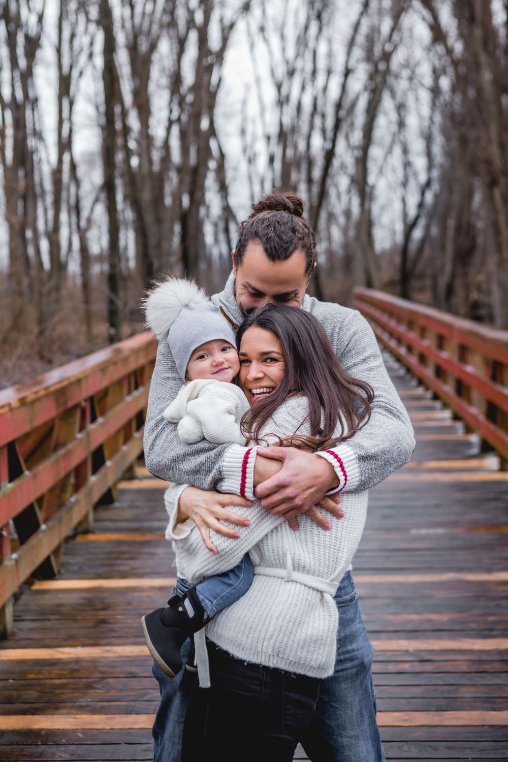 Family members share tender moments on a rustic wooden bridge in winter.