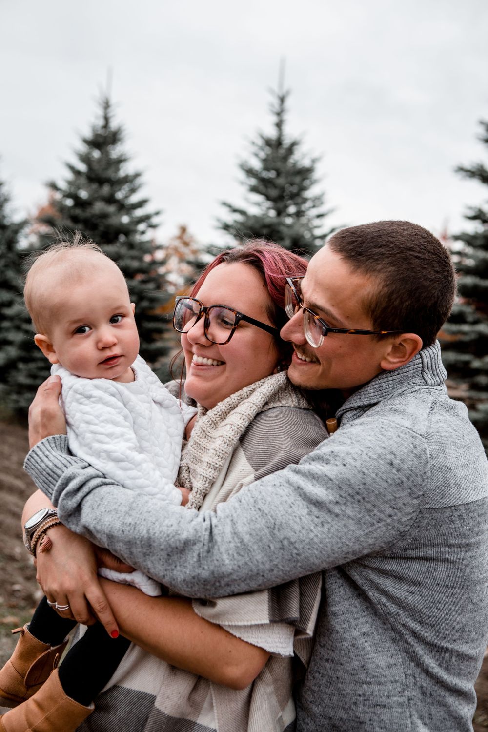 A family embraces while posing against evergreen trees in winter.