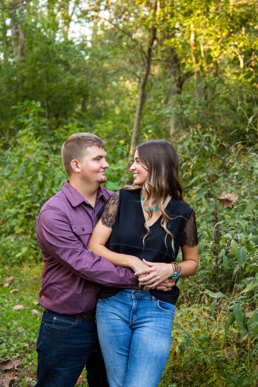 Romantic couple laughing together outdoors against a natural forest backdrop.