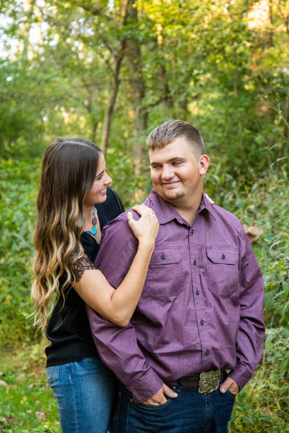 A couple shares playful moments in a wooded setting wearing purple and black casual attire.