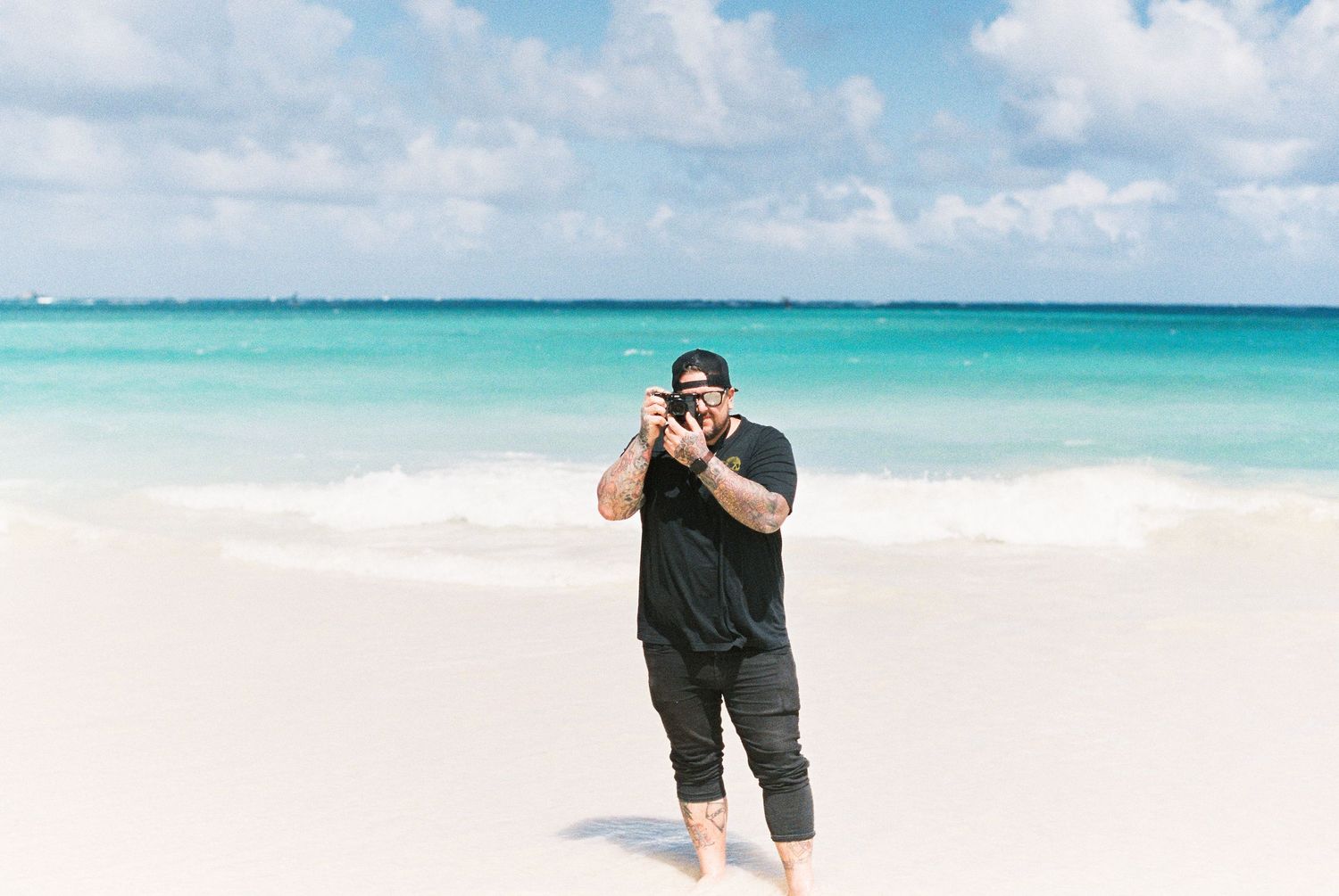 Person taking photographs on a pristine white sand beach with turquoise waters.