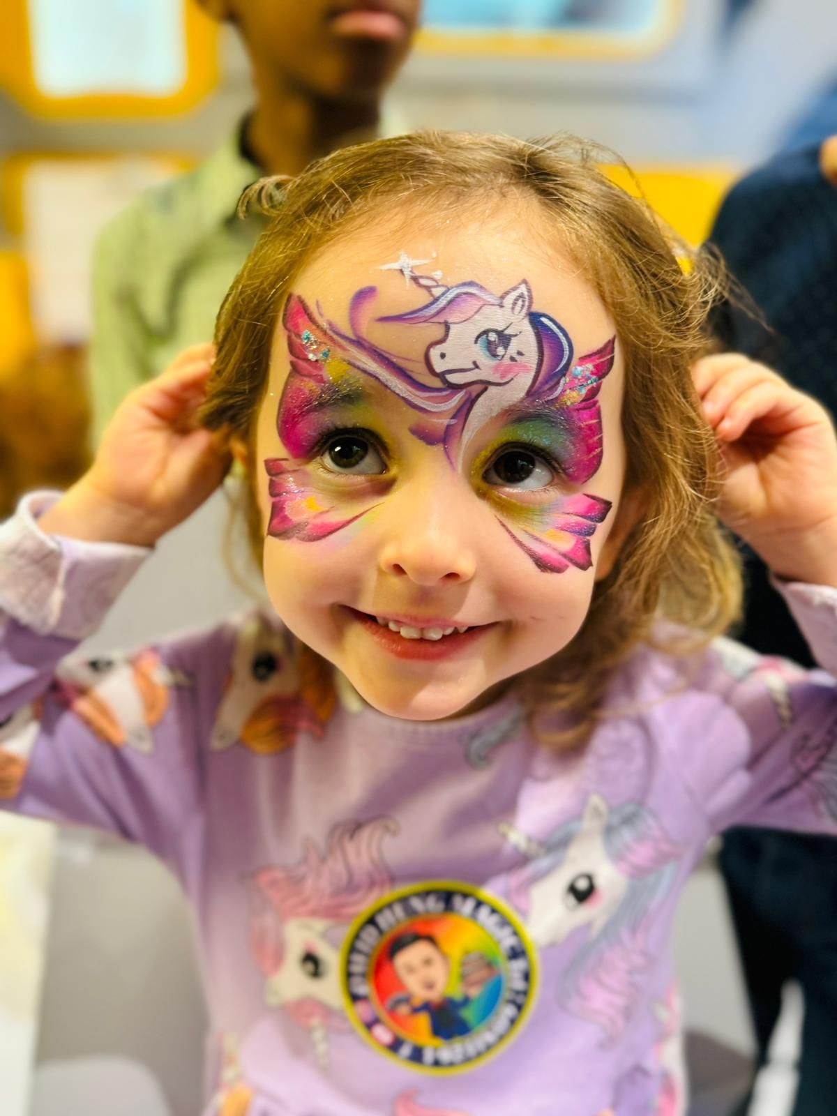 Colorful unicorn-themed face paint design with pink and purple swirls.