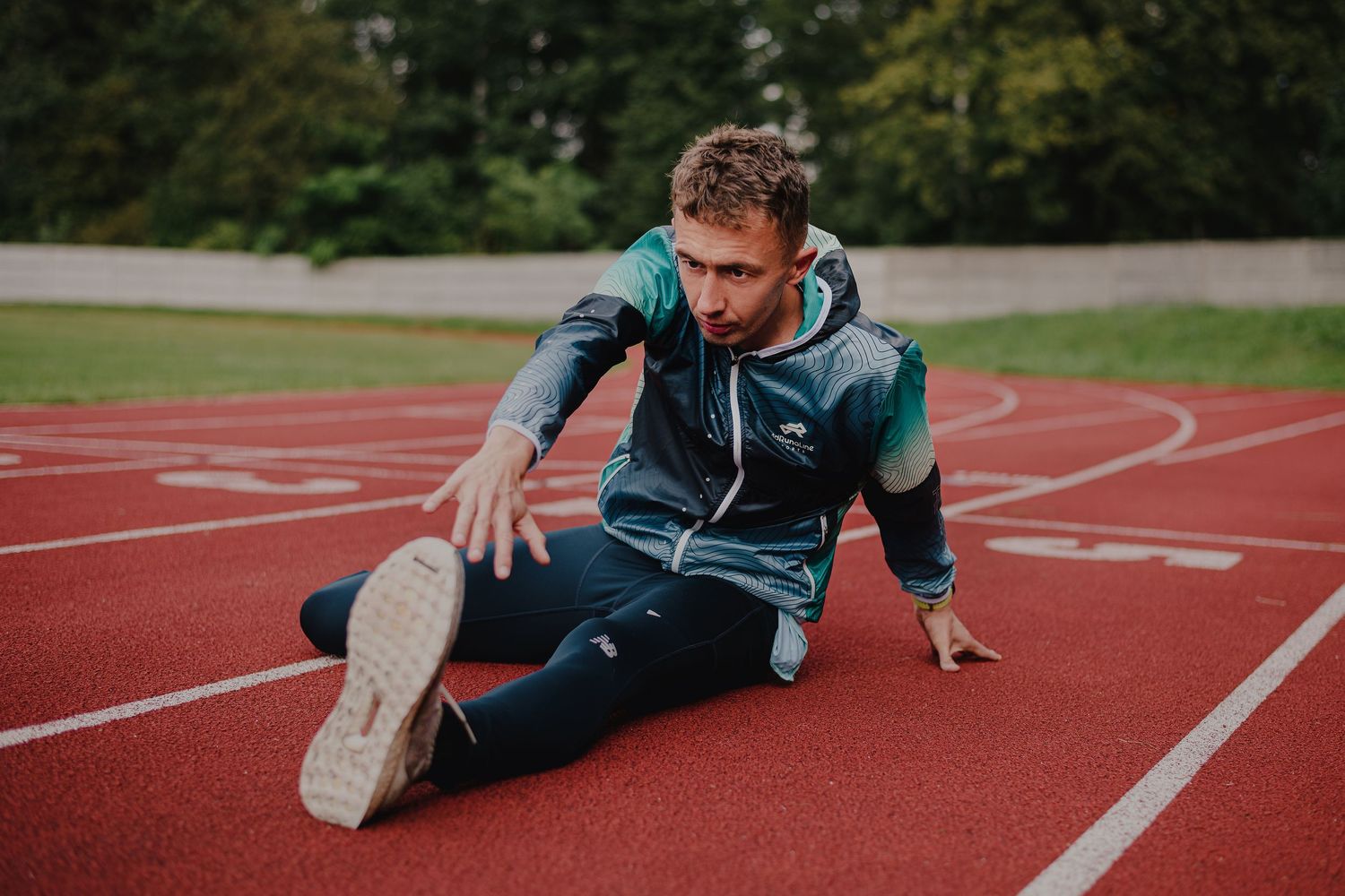 Athletic figure stretching and warming up on red running track before workout.