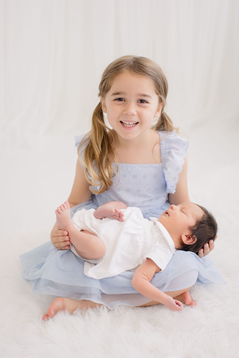 Two young siblings in light blue dress sitting together on white background.