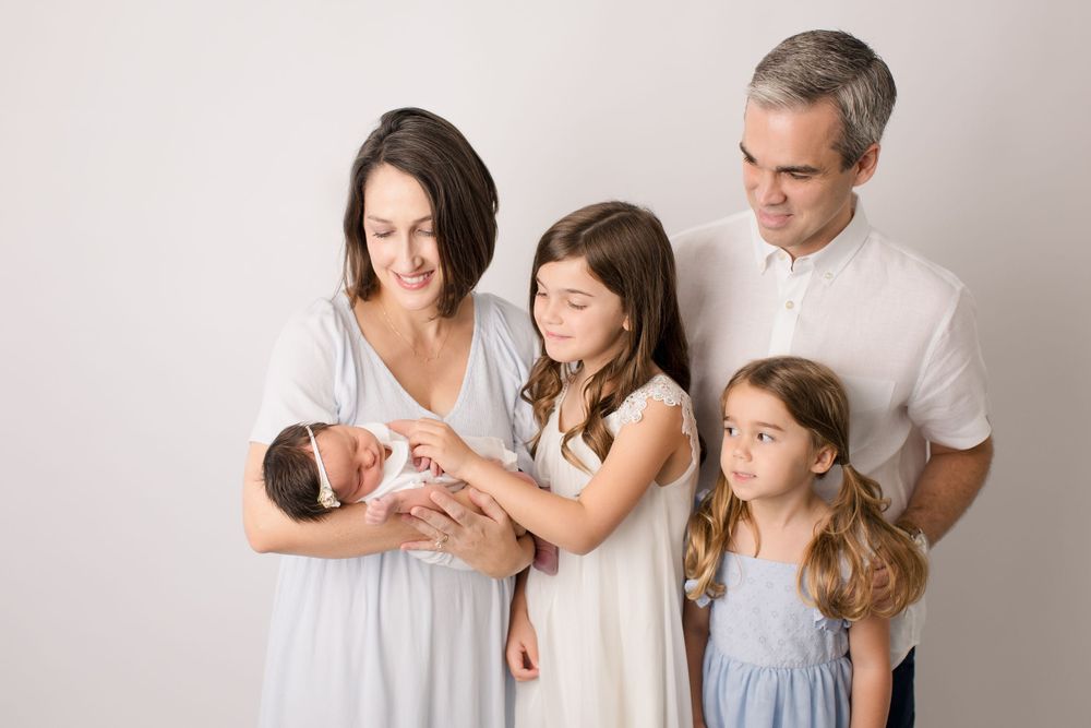 Family portrait with newborn baby in soft neutral tones against white background.