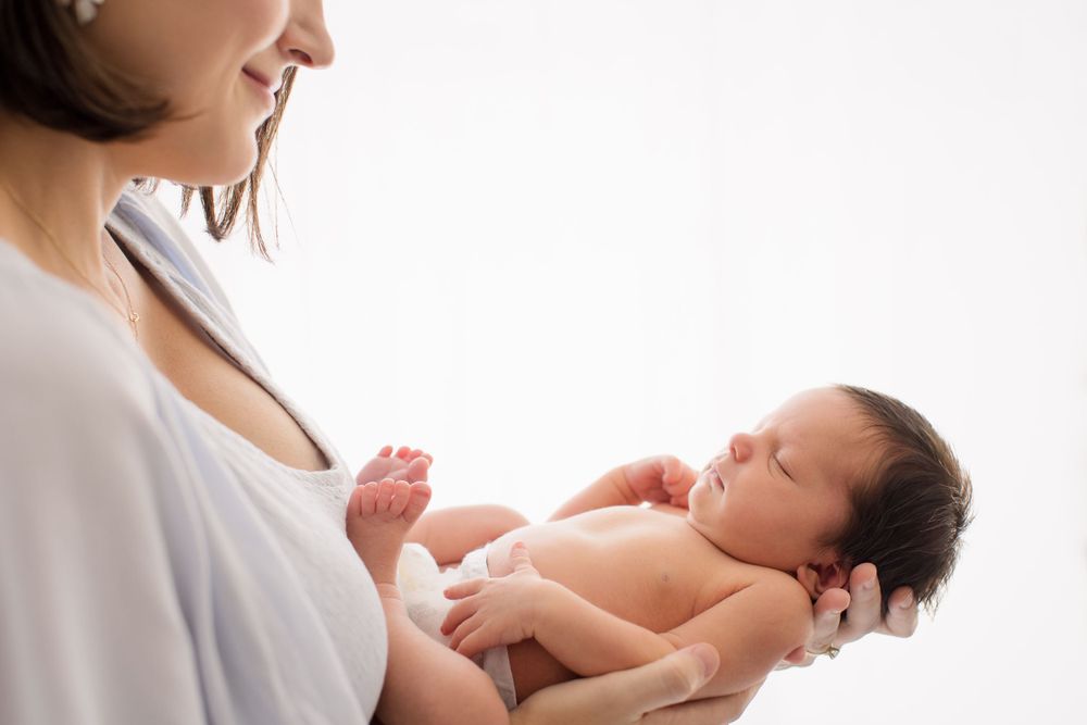 Side profile of person in white holding and gazing at peaceful newborn baby.