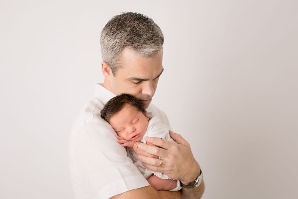 Tender moment between parent and sleeping newborn against light background.