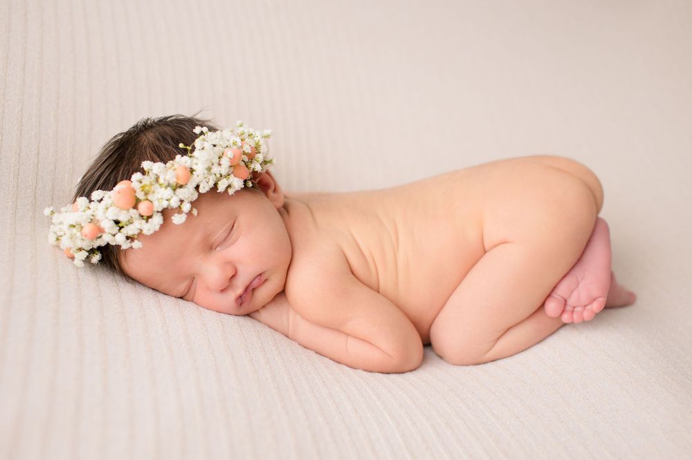 Sleeping newborn wearing delicate flower crown posed on white backdrop.