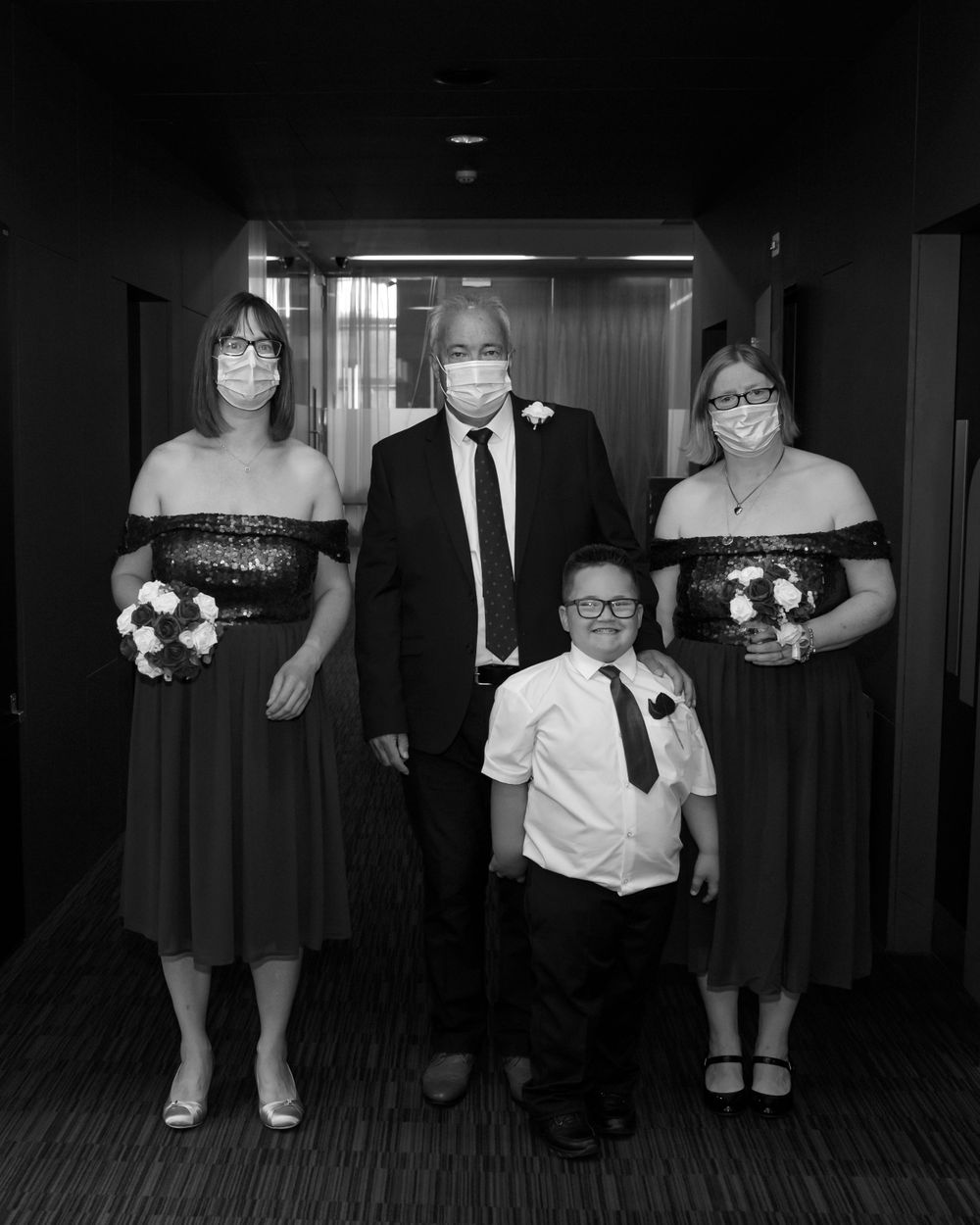Formal wedding party lineup in black and white against a dark background.