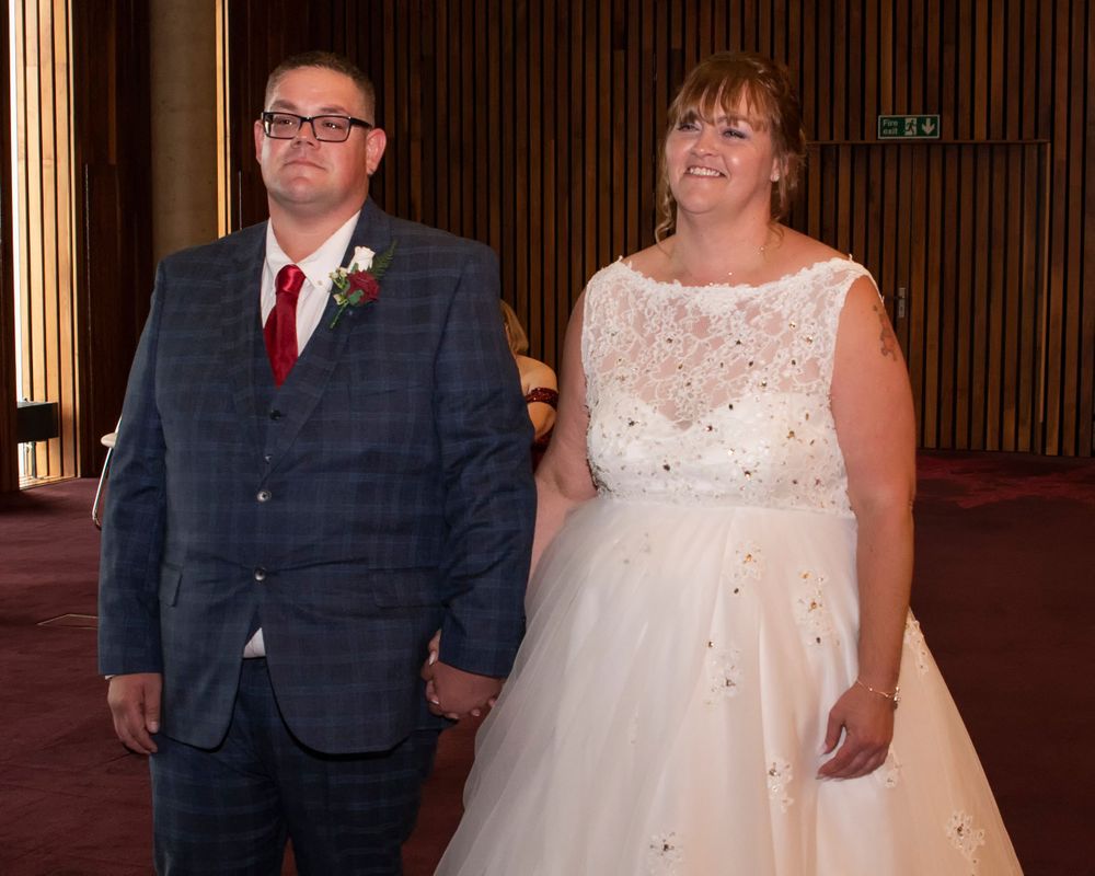 Wedding couple and party members in formal attire standing in an indoor venue.