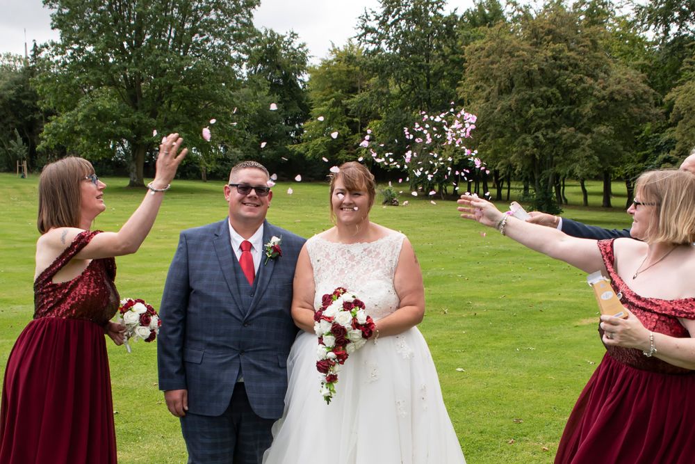 Wedding party poses on green lawn with burgundy bridesmaid dresses and white bridal gown.