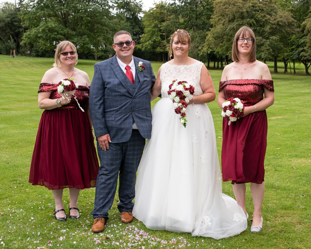Wedding group photo on grass with burgundy bridesmaids dresses and white bridal gown.