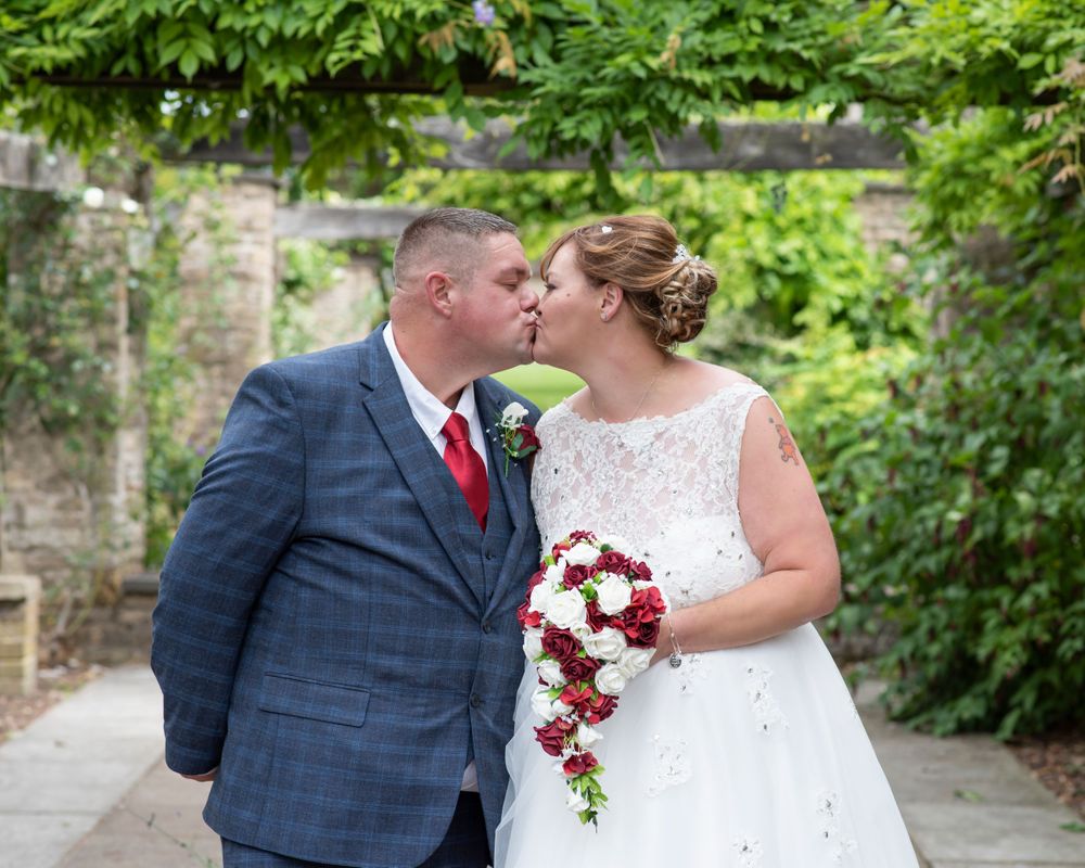 A couple in wedding attire embracing in a garden setting with lush greenery.