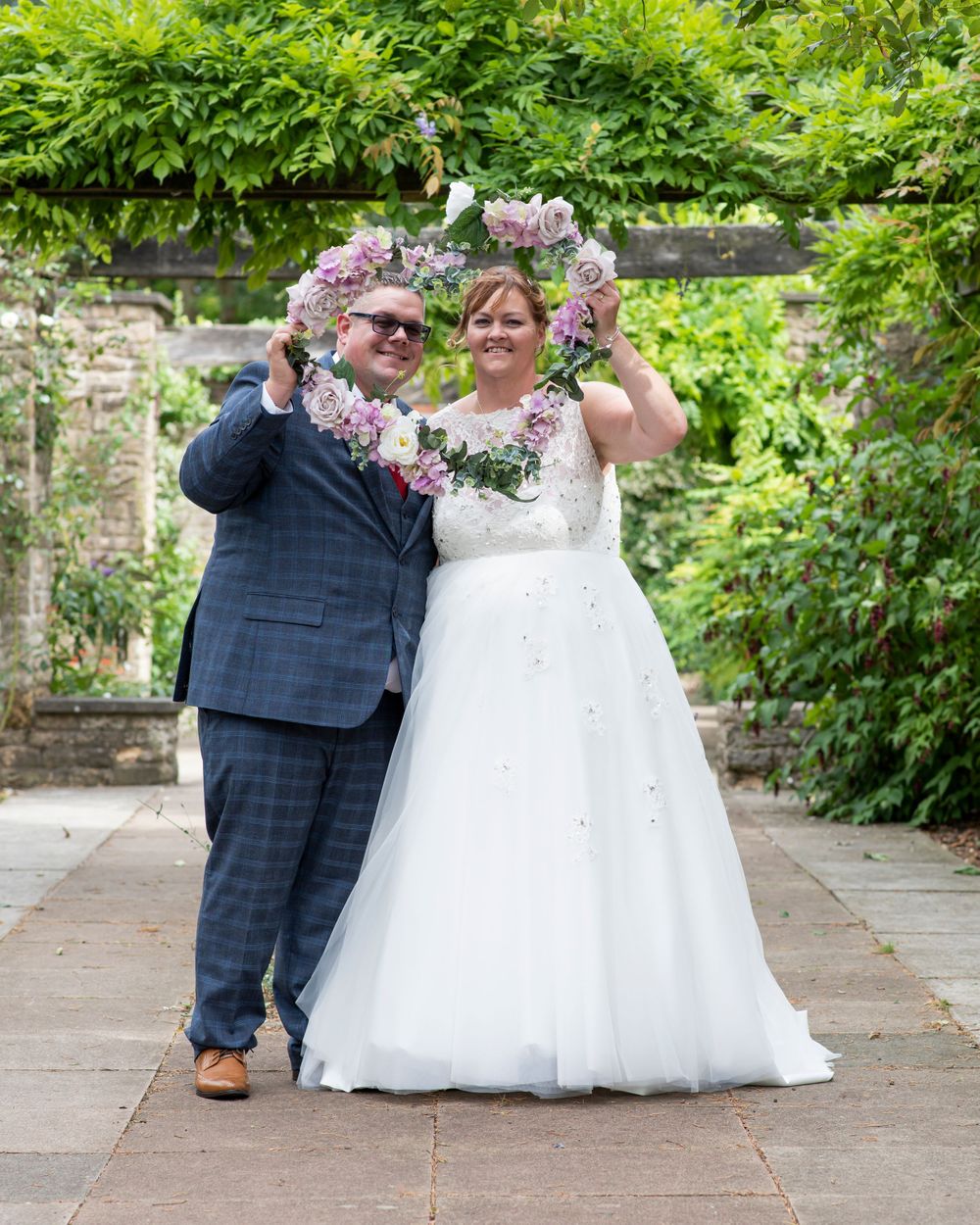 A romantic wedding moment captured in a garden with stone walls and vibrant foliage.