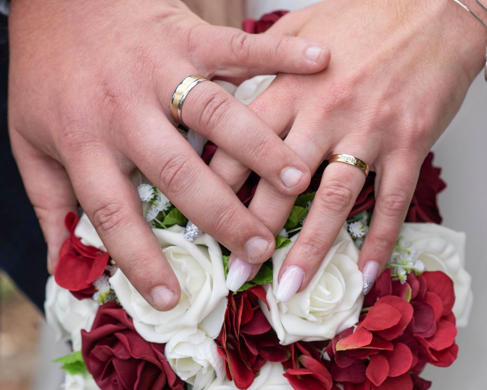 Close-up of hands holding a red and white rose wedding bouquet.