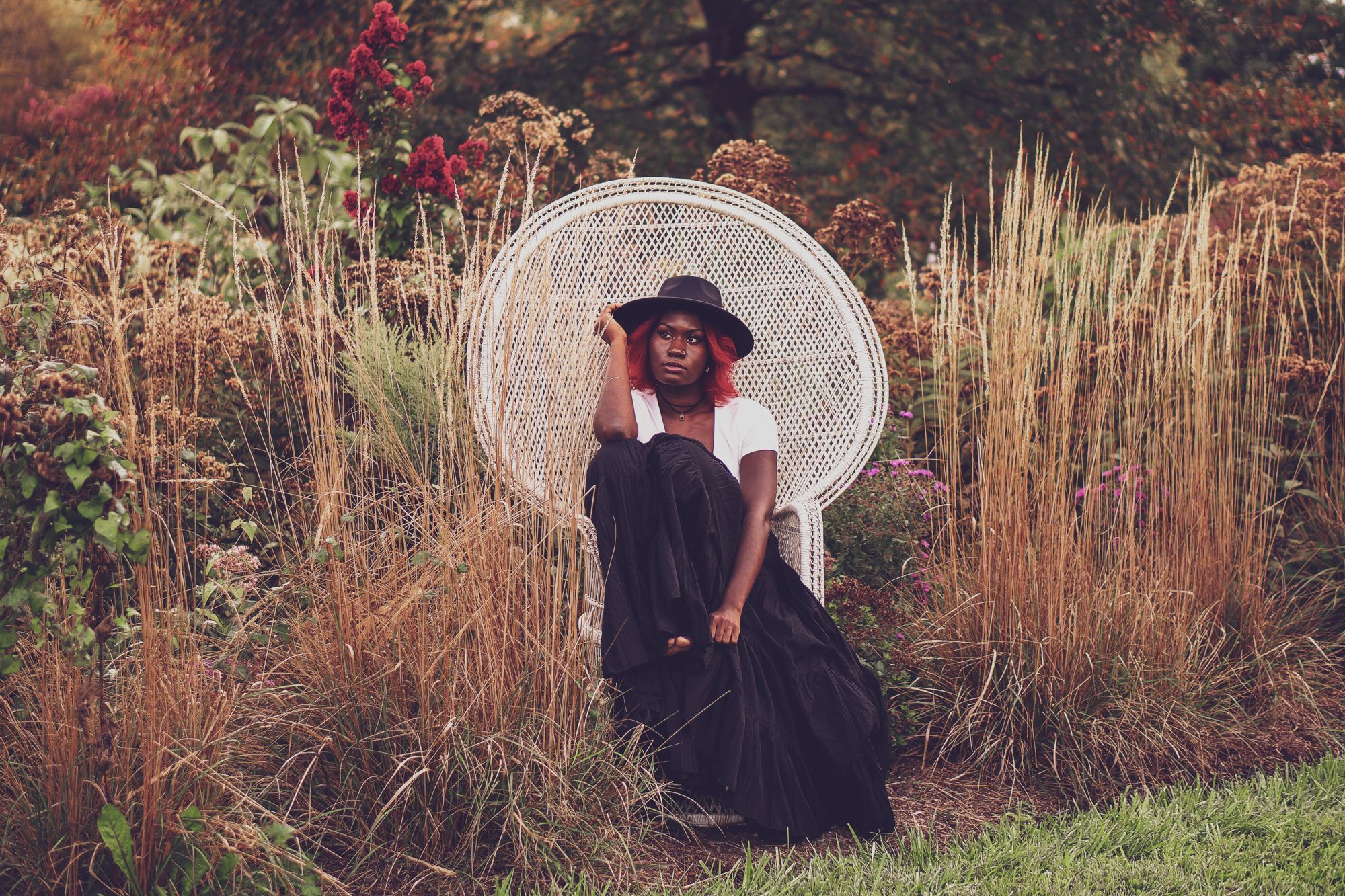 Captivating model sits in a wicker chair amongst a lush and gorgeous field of autumn colored scenery