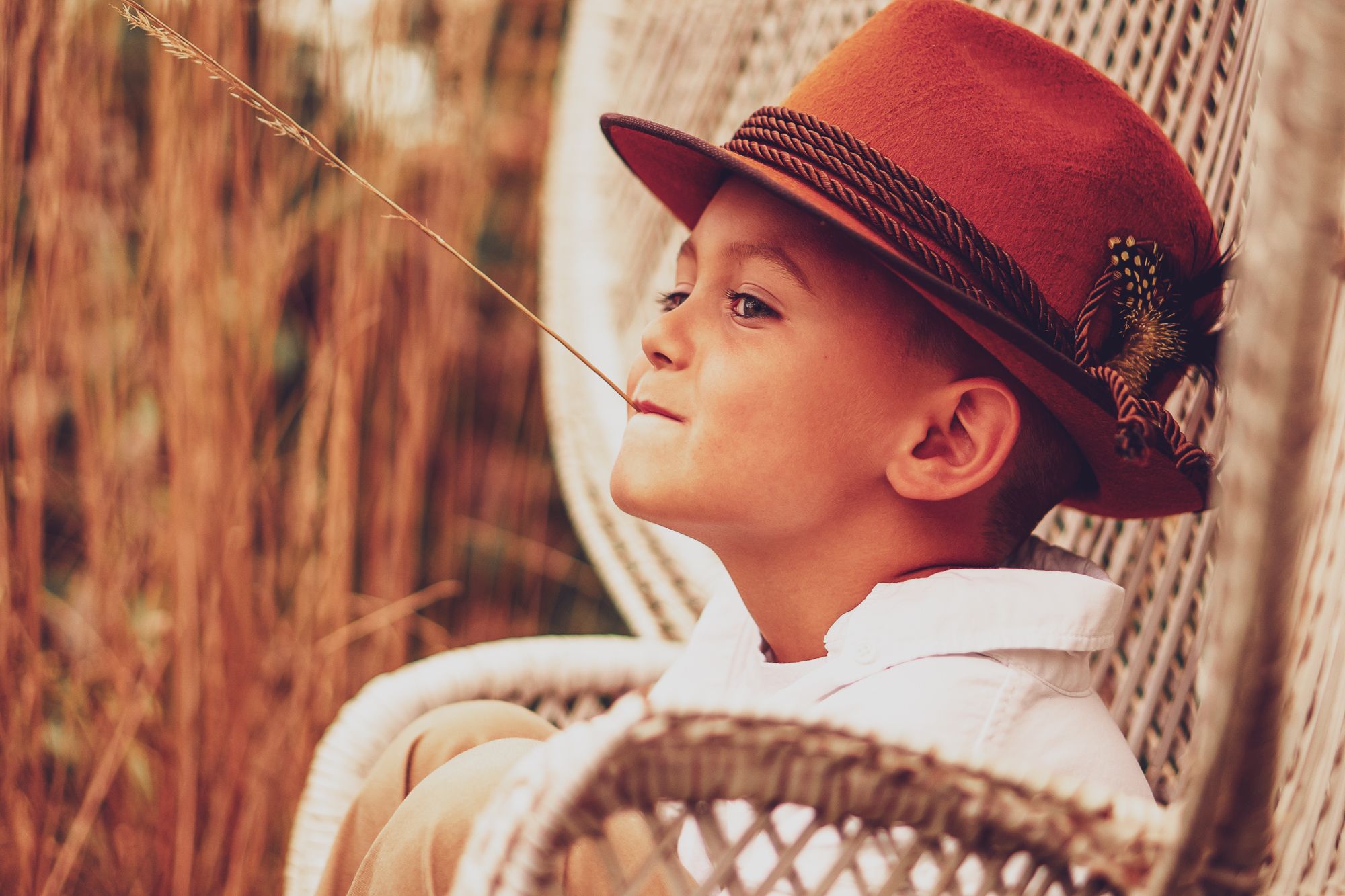 Adorable young man sits in a wicker chair in this dreamy warm toned bohemian image